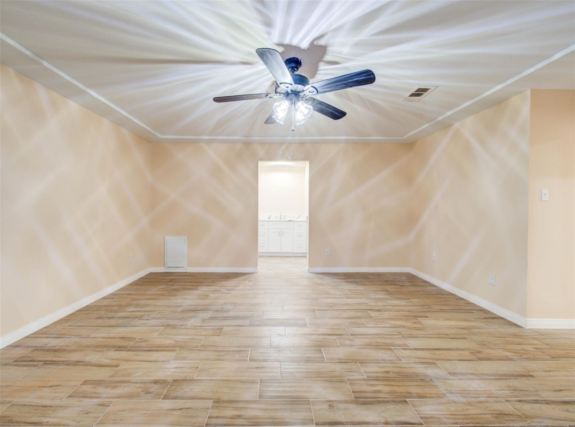 13526 Sherwood Street, Sugar Land, TX 77498 Spacious room with wood-like flooring, neutral walls, and a ceiling fan with lights. There's a doorway leading to a brightly lit area with cabinets.