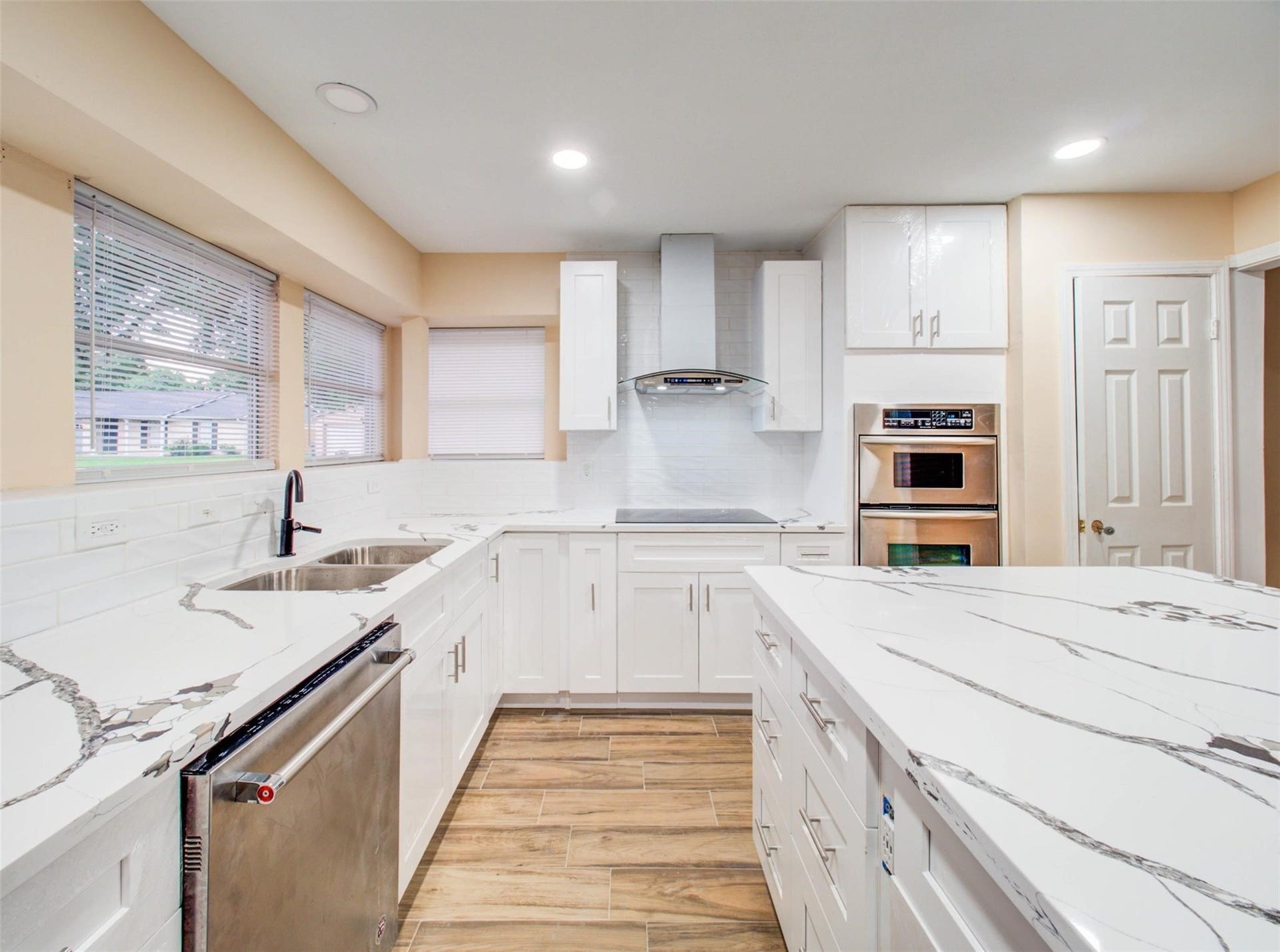 13526 Sherwood Street, Sugar Land, TX 77498 This kitchen features modern white cabinetry, granite countertops, stainless steel appliances, and wood-look flooring. It has ample natural light from large windows and a sleek, contemporary design.