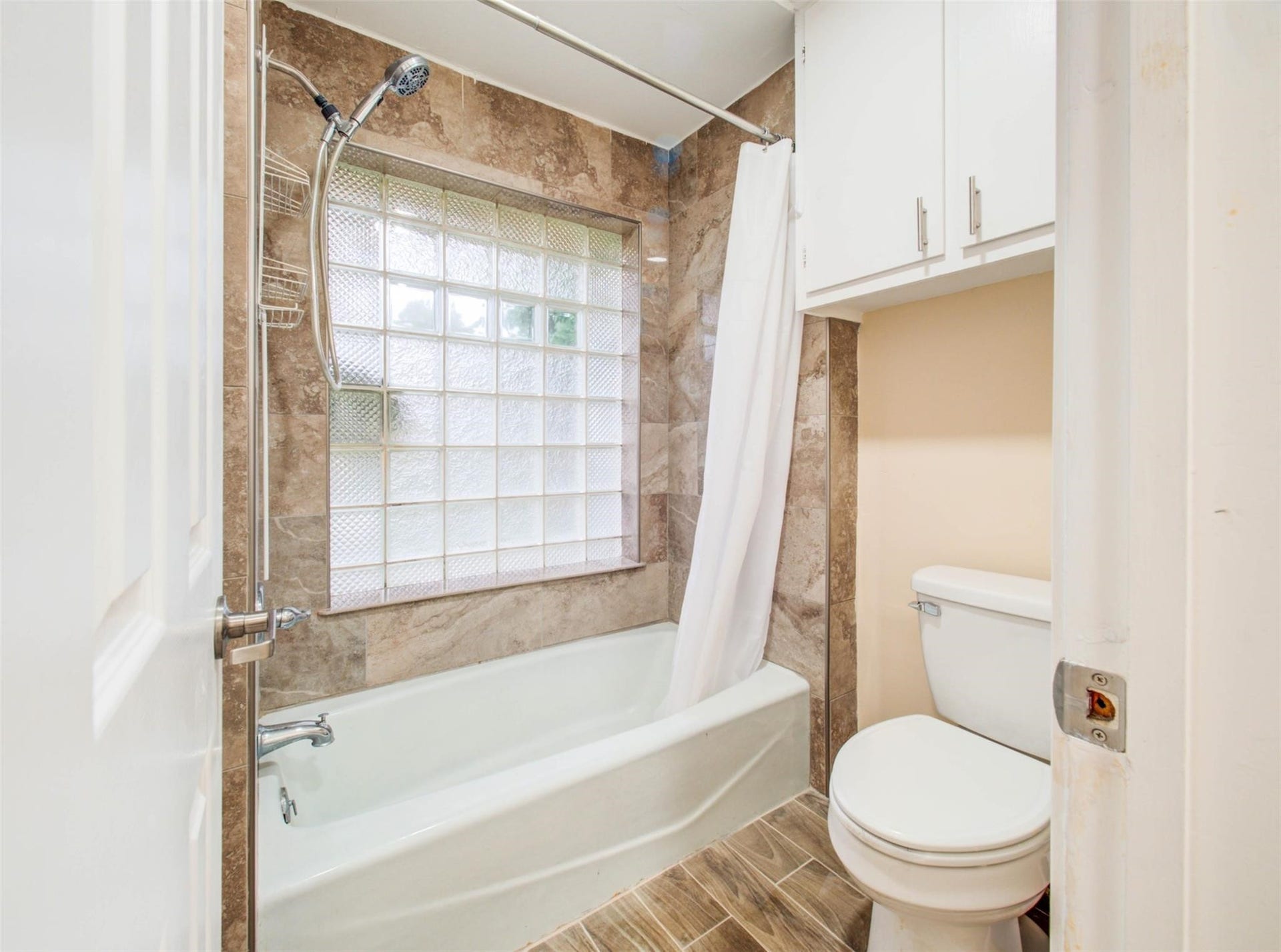13526 Sherwood Street, Sugar Land, TX 77498 Compact bathroom with a bathtub and shower combo, featuring a glass block window for natural light. It has white cabinetry, tiled walls, and a floor designed for easy maintenance.