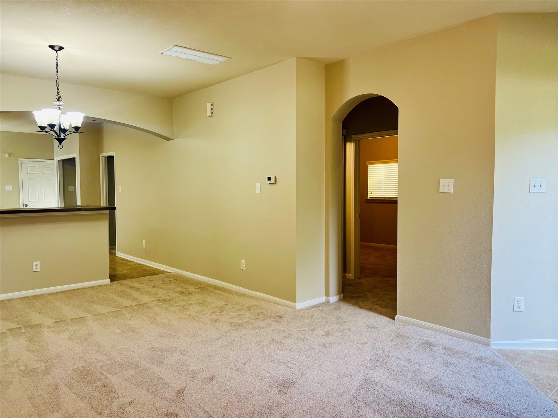 1721 Claremont Garden Circle, Houston, TX 77047 Spacious living area with plush carpet flooring, warm neutral walls, and a charming arched doorway leading to additional rooms. The open layout includes a modern light fixture and a partial view of the kitchen with a high countertop.