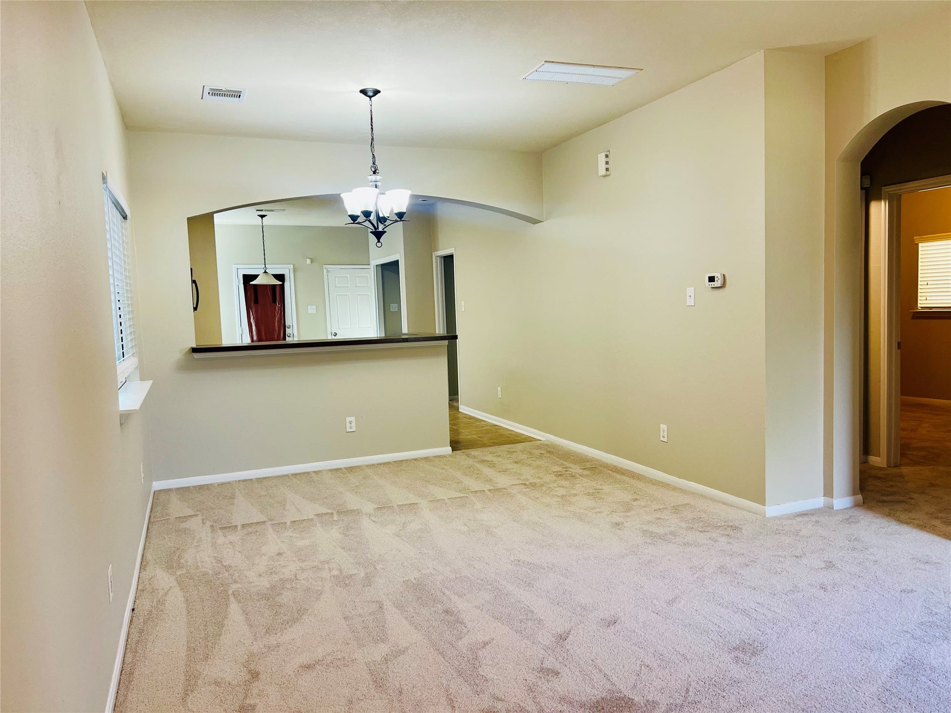 1721 Claremont Garden Circle, Houston, TX 77047 Spacious living area with plush carpeting, neutral walls, and an elegant arched opening leading to the kitchen, featuring modern light fixtures and a convenient breakfast bar.