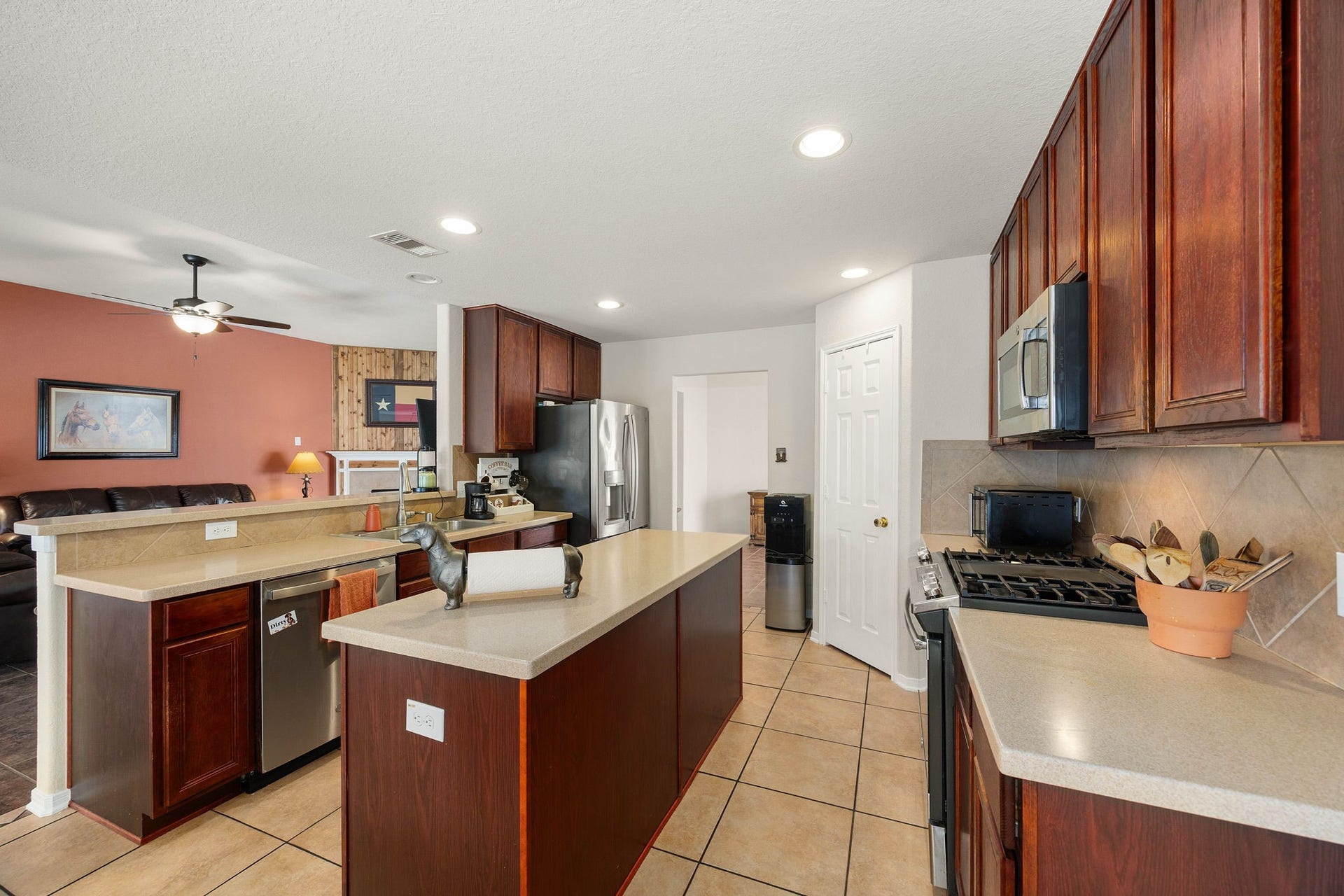 Well-designed kitchen featuring rich wood cabinetry, durable tile flooring, and matching stainless steel appliances, including a built-in microwave and gas range. A central island provides extra workspace, while the raised breakfast bar bar connects the space to the family room for an open, interactive feel.