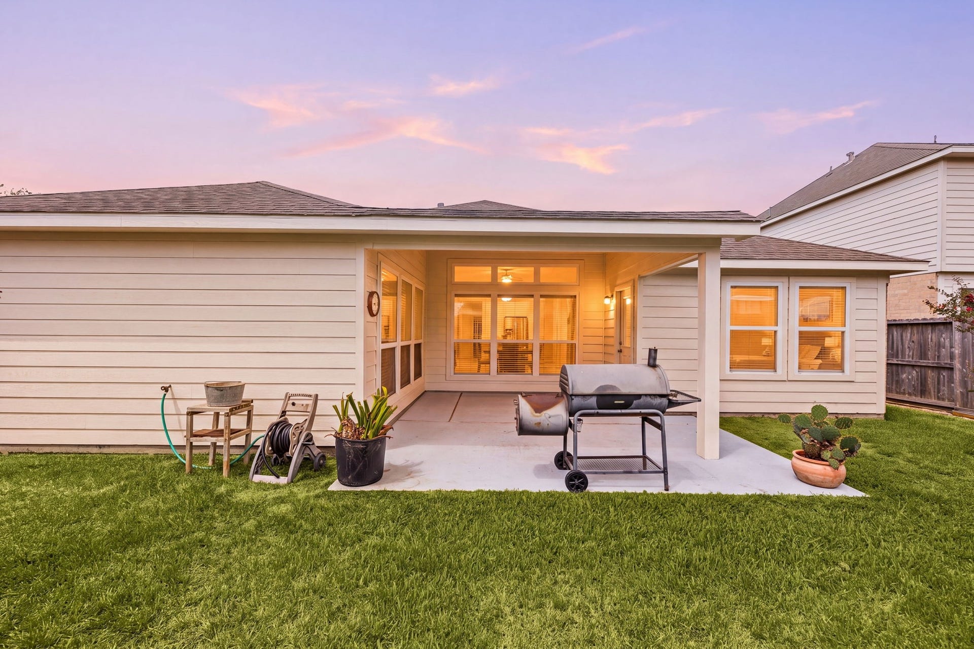 Fully fenced backyard showcasing a clear view of the covered back patio and a spacious lawn area.