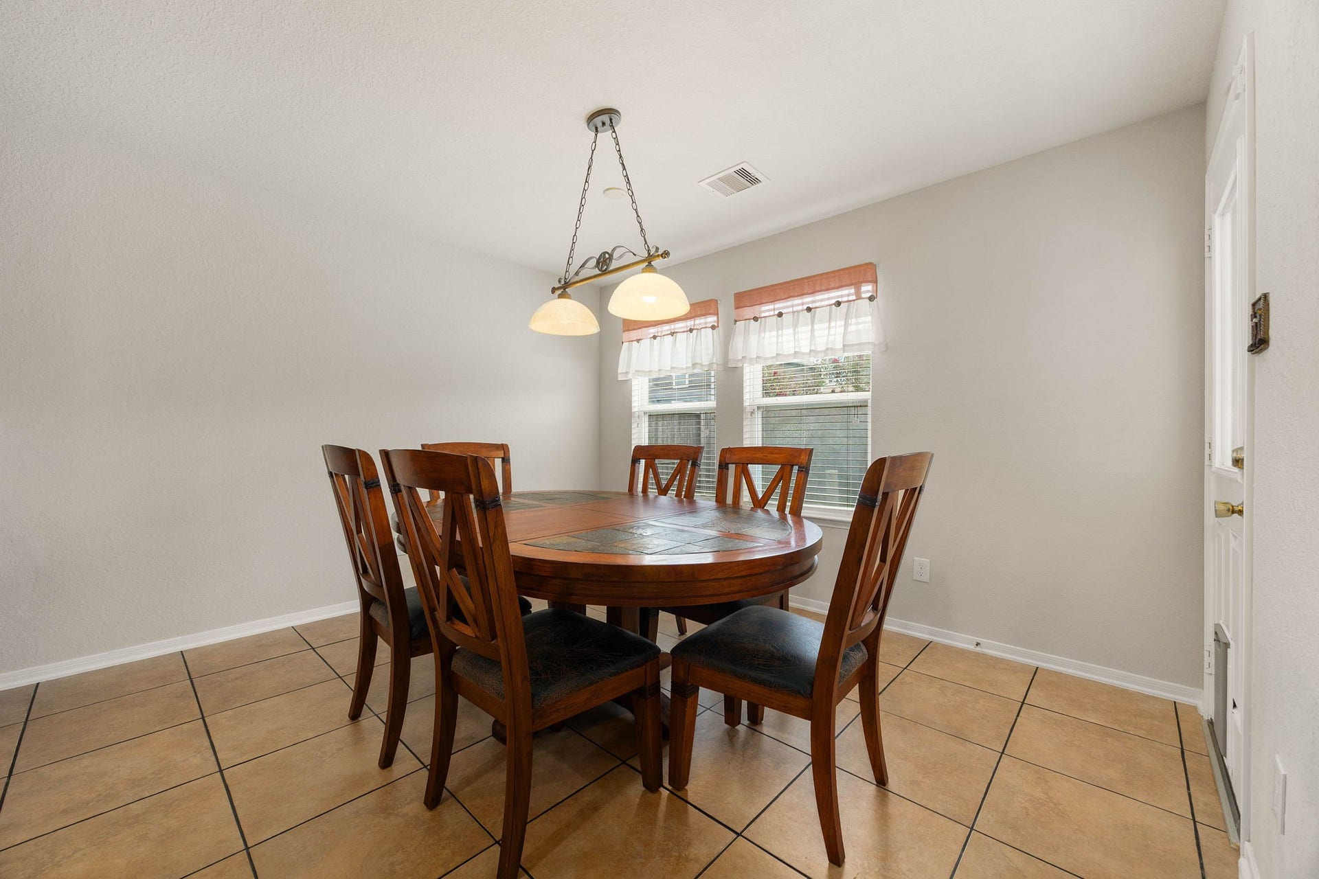 Bright and sunny breakfast nook featuring low-maintenance tile flooring and a distinctive hanging island light fixture. Twin windows fill the space with comfortable daylighting, while the adjacent exterior door provides convenient, direct access to the back patio and yard.