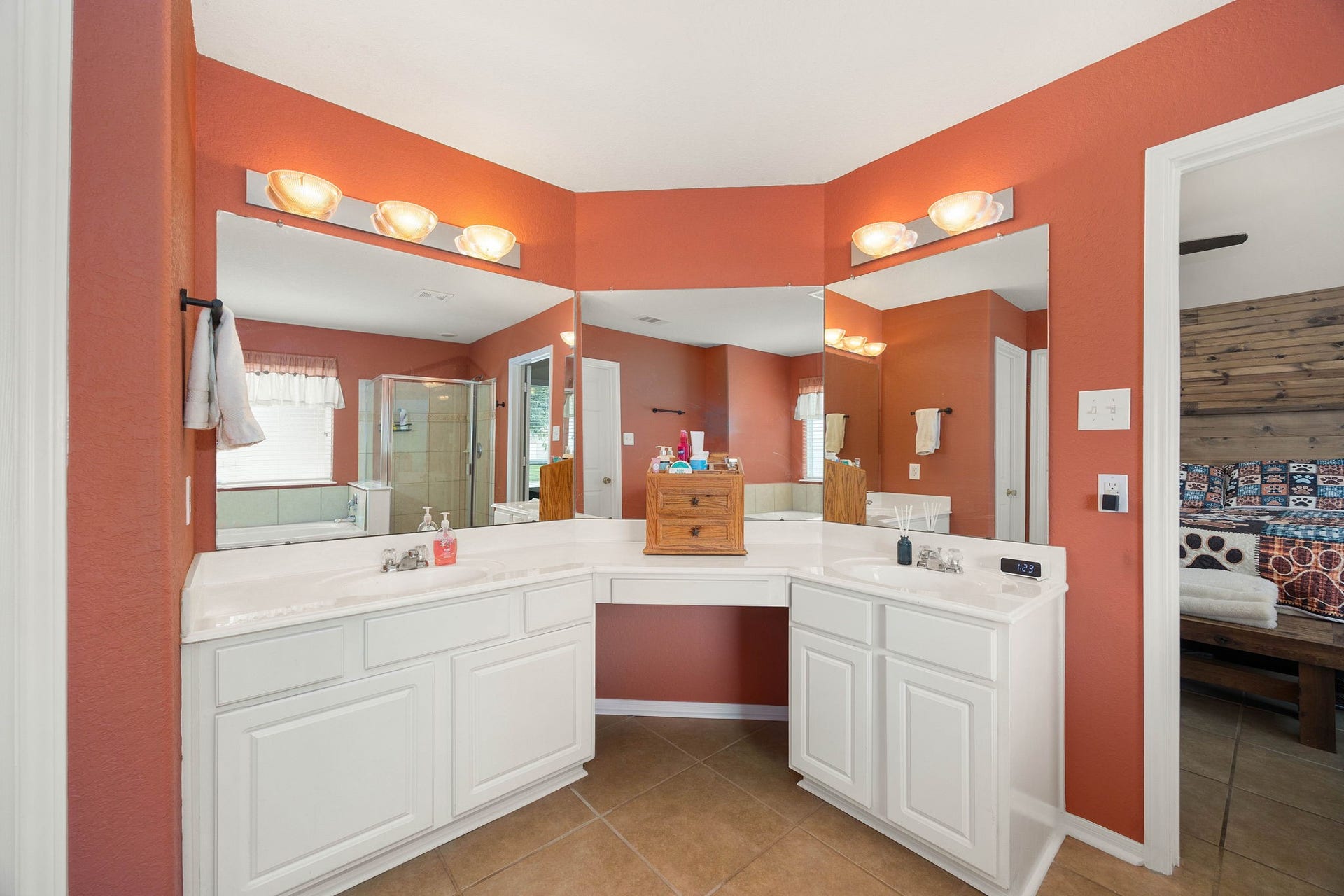 Generous primary en-suite bathroom featuring an expansive double vanity with two separate sinks and a dedicated sit-down makeup station. White cabinetry provides plenty of storage space, while large mirrors and multi-bulb lighting fixtures keep the room bright.