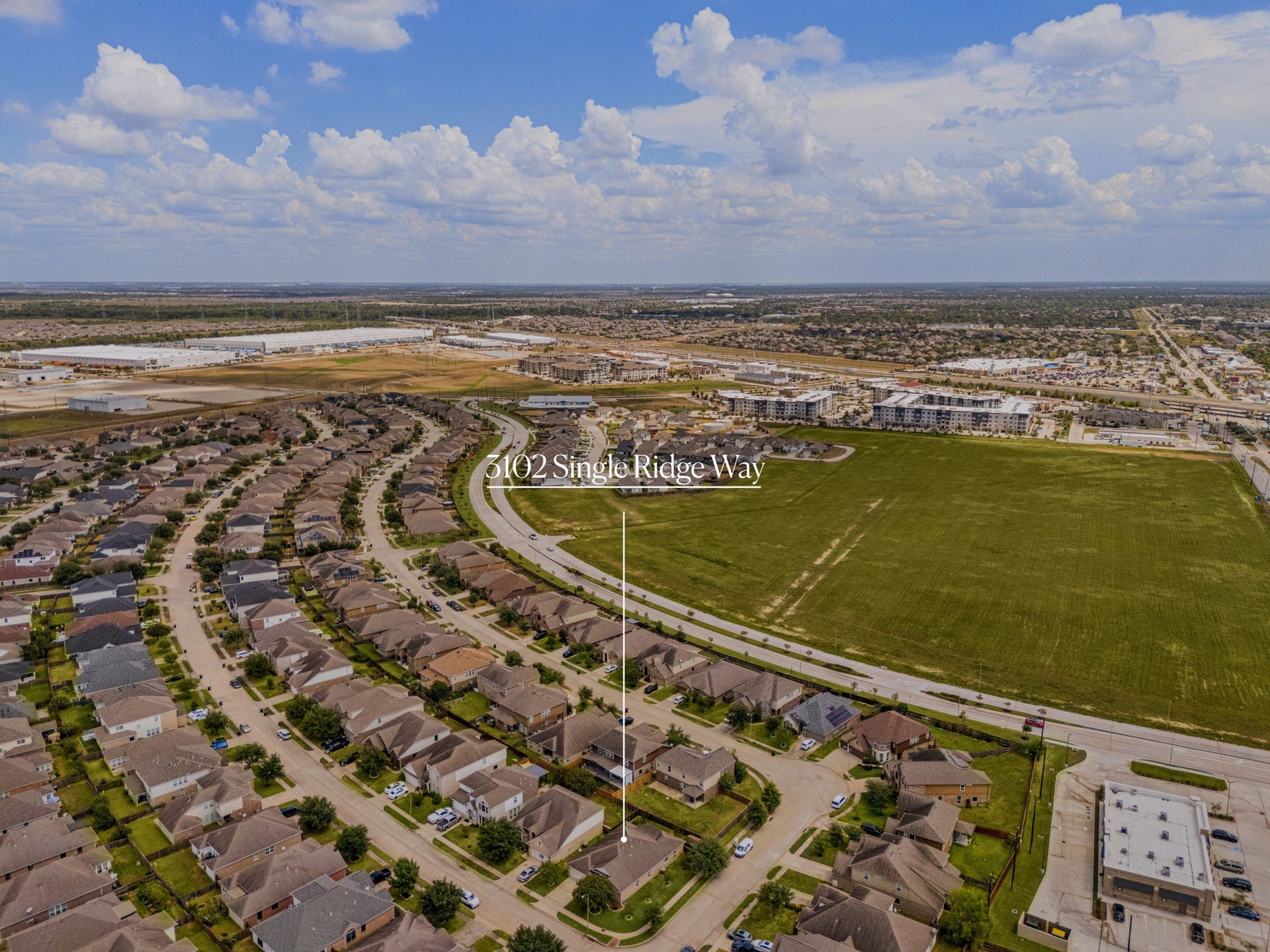 High-altitude aerial view pinpointing 3102 Single Ridge Way, emphasizing its strategic location within a beautifully developed neighborhood. The perspective highlights the property's proximity to a sweeping green space and showcases the easy connectivity to nearby main roads and commercial developments.