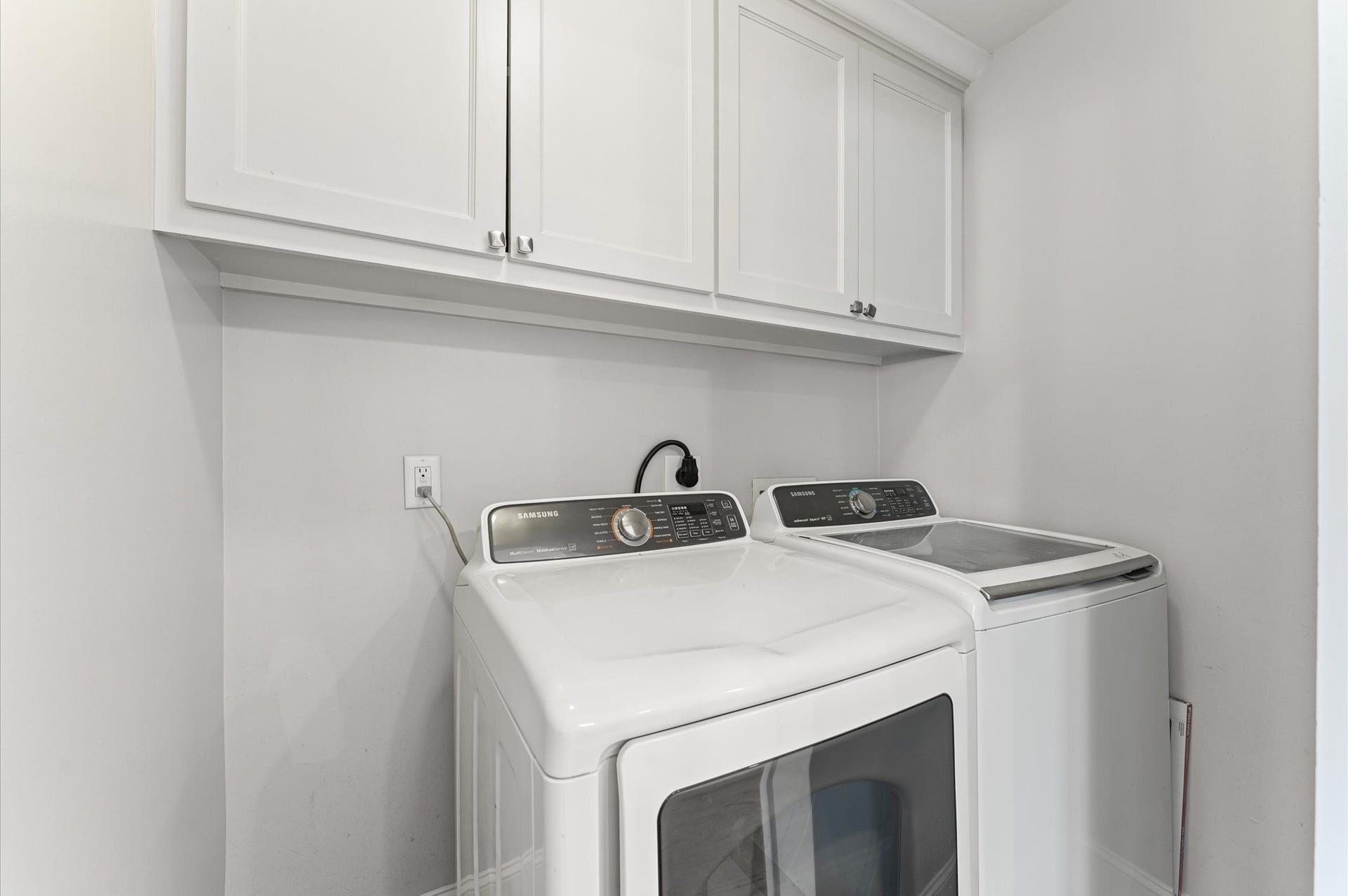 1204 Shearn Street, Houston, TX 77007 This photo showcases a compact laundry room with a modern washer and dryer set, featuring overhead white cabinets for storage. The space is clean and efficiently organized.