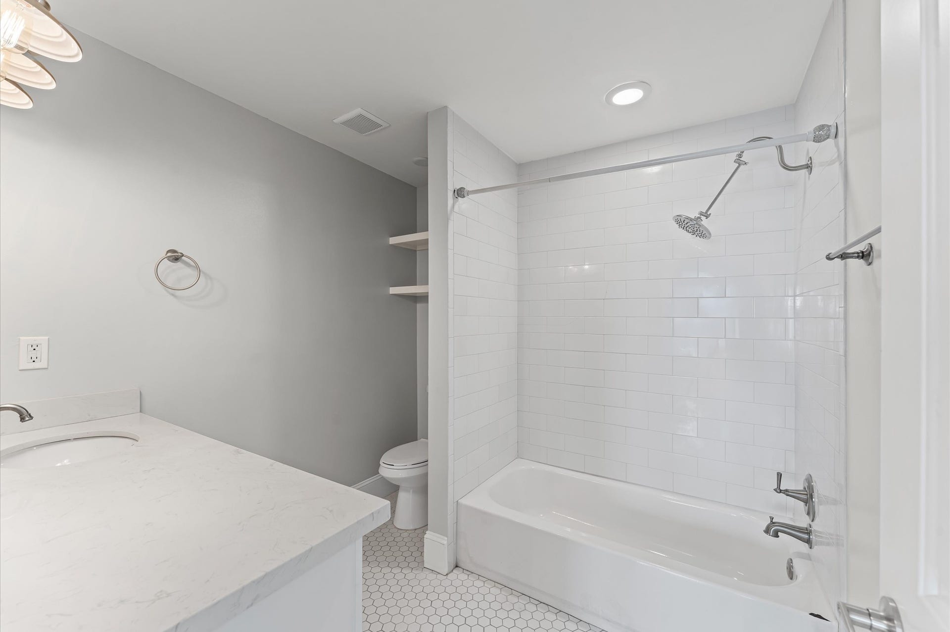 1204 Shearn Street, Houston, TX 77007 This modern bathroom features a sleek design with a white subway-tiled shower, hexagonal floor tiles, and a spacious vanity. Ample lighting and built-in shelves add functionality and style.