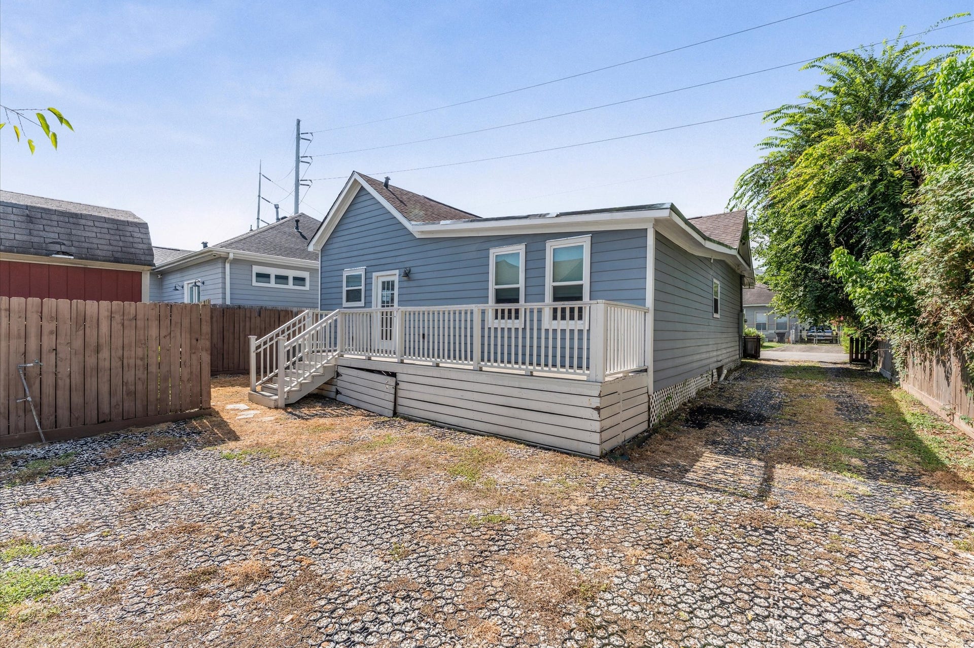 1204 Shearn Street, Houston, TX 77007 This photo showcases the back exterior of a charming blue house with a small deck and steps leading to a fenced yard. The yard features a gravel and grass area, ideal for low maintenance.