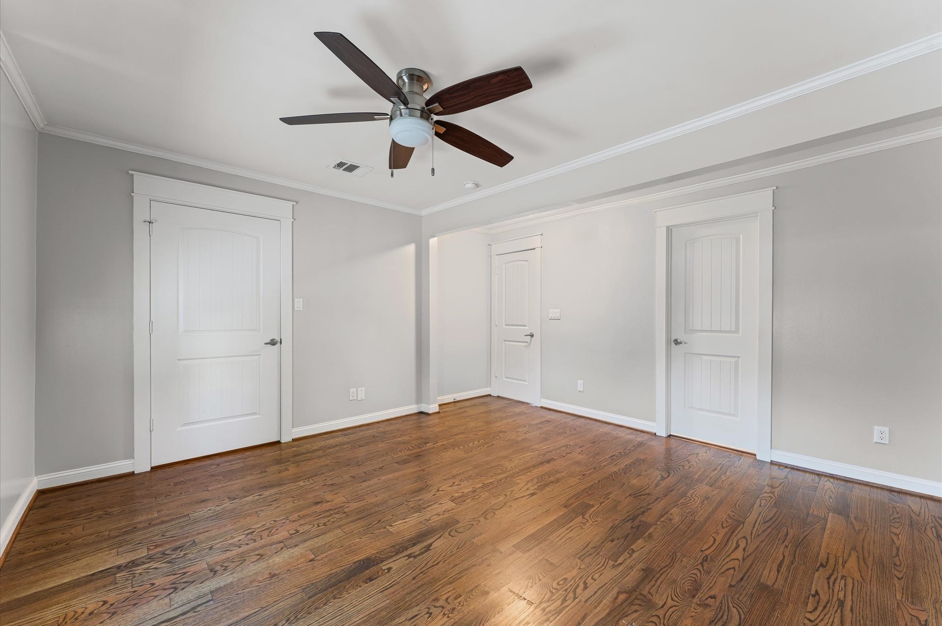1204 Shearn Street, Houston, TX 77007 This room features polished hardwood floors, neutral gray walls, white trim, and a ceiling fan, with multiple doors for easy access and storage.