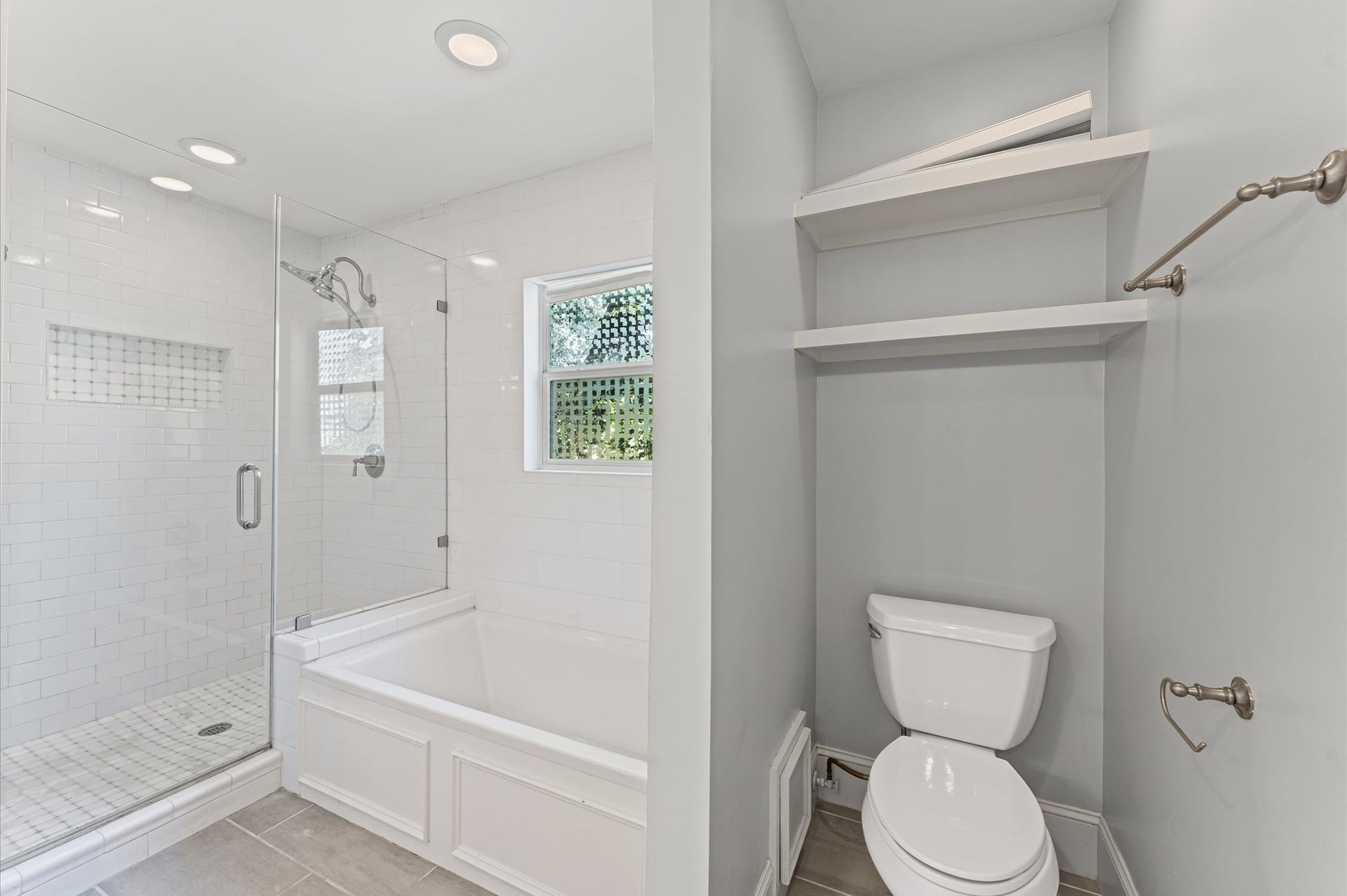 1204 Shearn Street, Houston, TX 77007 Modern bathroom featuring a glass-enclosed shower and bathtub combo, with subway tile walls. There's a small window for natural light, a toilet with shelving above, and sleek fixtures.