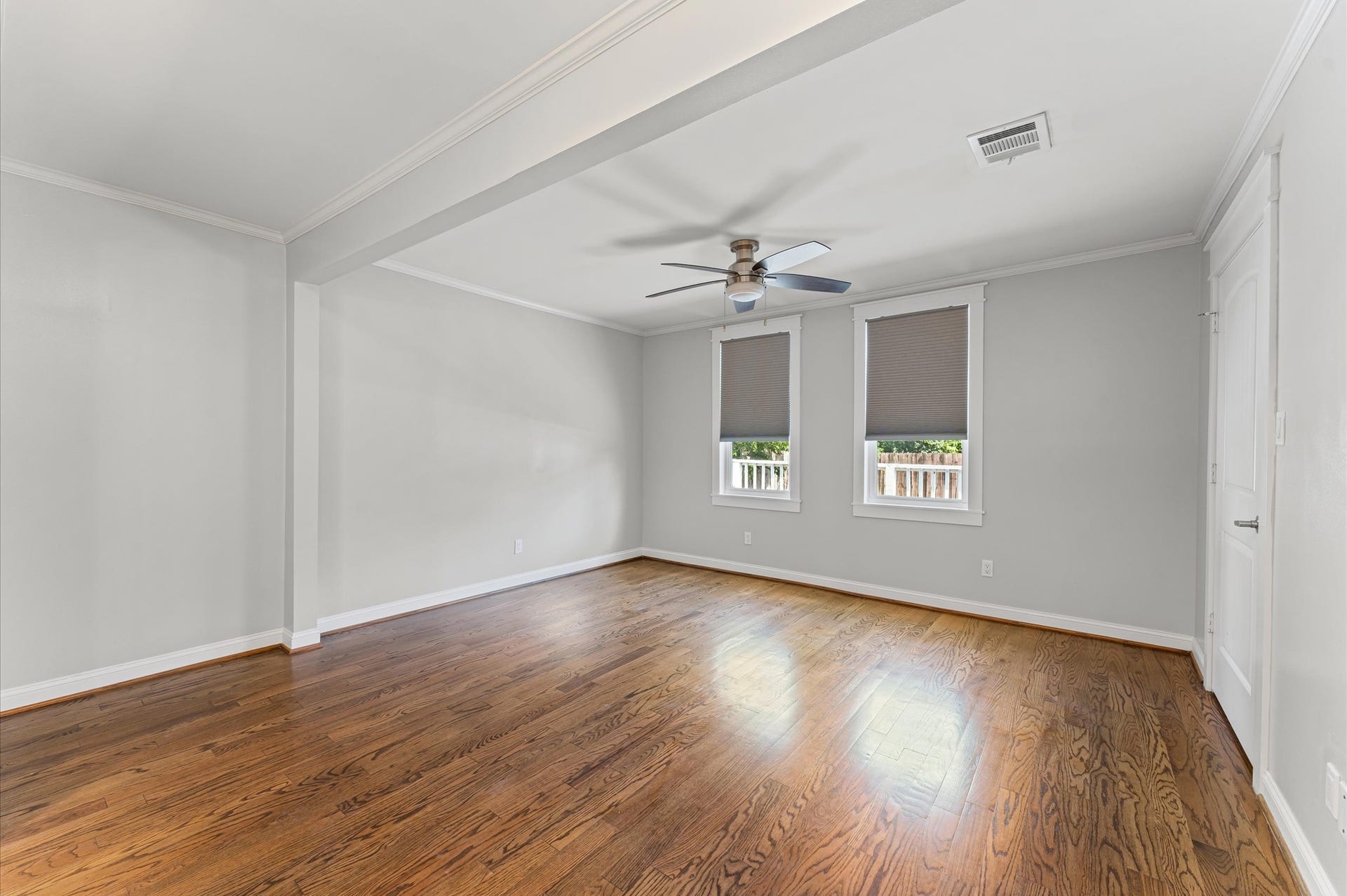 1204 Shearn Street, Houston, TX 77007 Spacious, bright room with hardwood floors, neutral walls, a ceiling fan, and two windows with blinds. Ideal for a bedroom or living space.