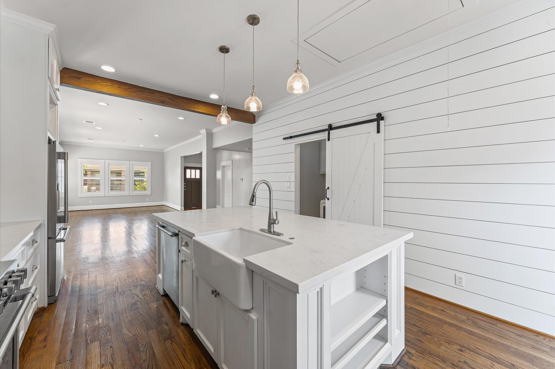 1204 Shearn Street, Houston, TX 77007 This bright kitchen features white shiplap walls, a large island with a farmhouse sink, and pendant lighting. It opens to a spacious living area with hardwood floors and a sliding barn door.