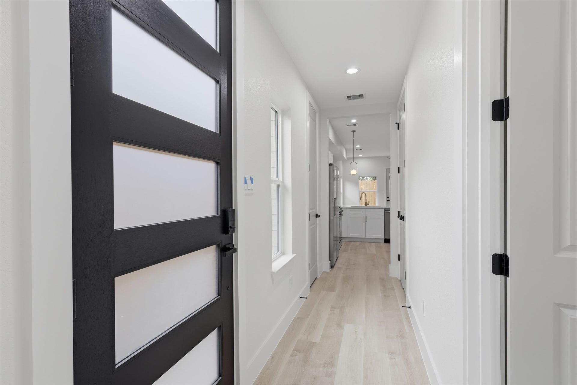 3201 Berry Street, #A/B, Houston, TX 77004 Sleek modern entryway featuring a stylish black door and bright, inviting hallway leading to an open kitchen with contemporary fixtures.