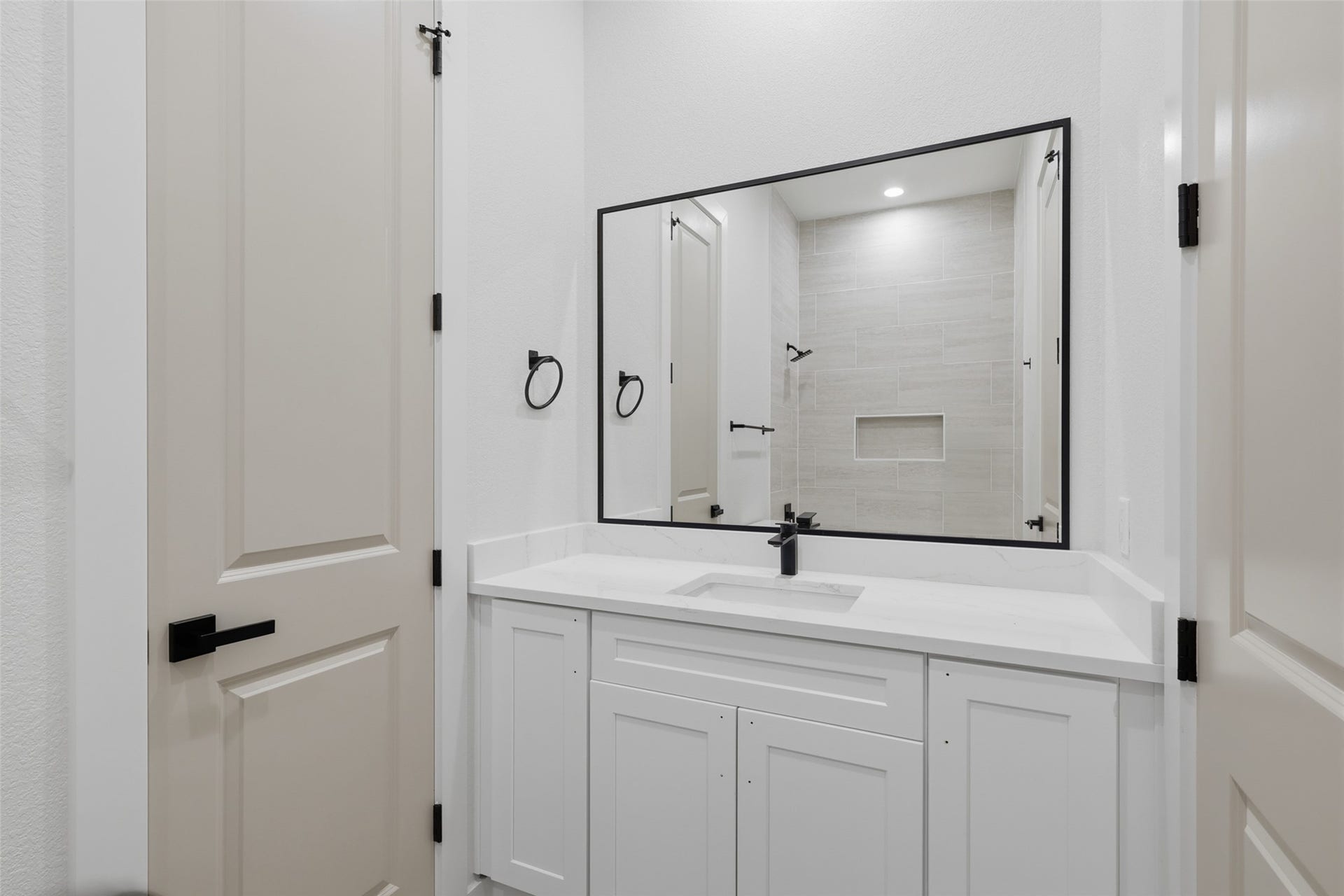 3201 Berry Street, #A/B, Houston, TX 77004 Elegant bathroom featuring a sleek white vanity with a modern black-framed mirror, complemented by a spacious tiled shower area with a built-in shelf.