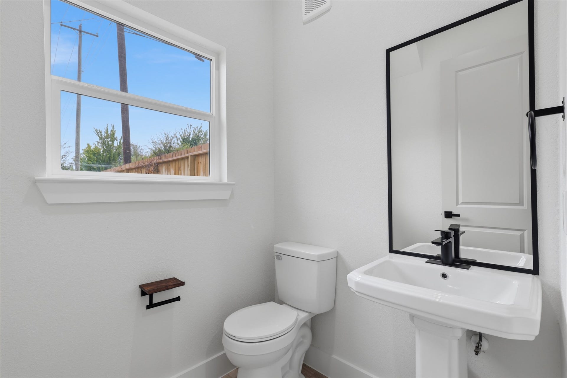 3201 Berry Street, #A/B, Houston, TX 77004 Bright and modern 1,2 bath in the front entrance on the first floor, featuring a sleek pedestal sink, large mirror, and natural light streaming through the window.