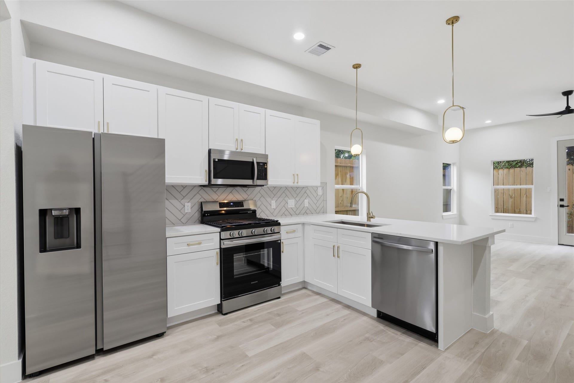 3201 Berry Street, #A/B, Houston, TX 77004 Sleek modern kitchen featuring stainless steel appliances, elegant white cabinetry, and a spacious L-shaped island with pendant lighting, perfect for entertaining.