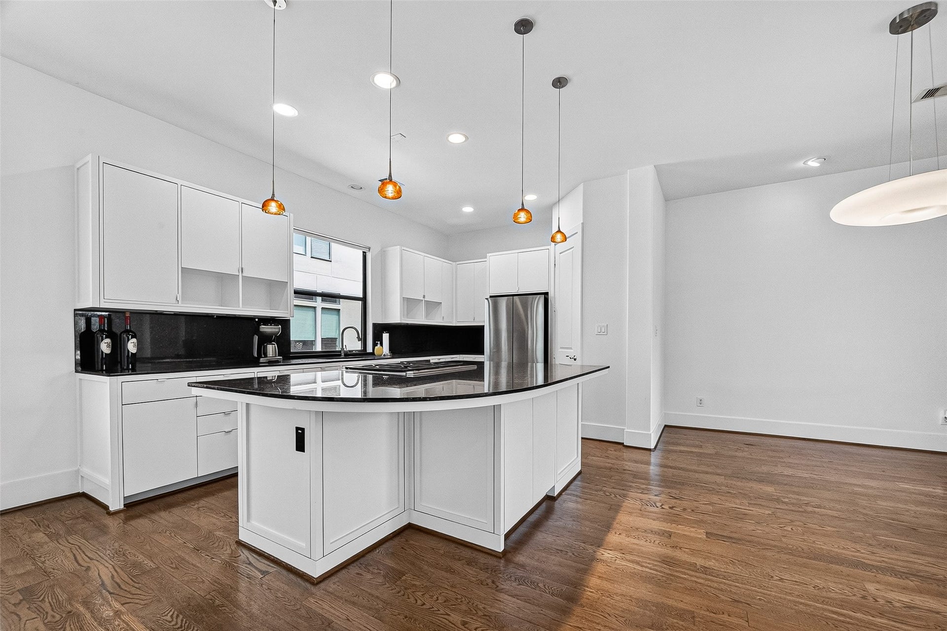 1110 Autrey Street, #C, Houston, TX 77006 Modern kitchen with sleek white cabinetry, a spacious island with dark countertops, and elegant pendant lighting, all set against warm hardwood floors.