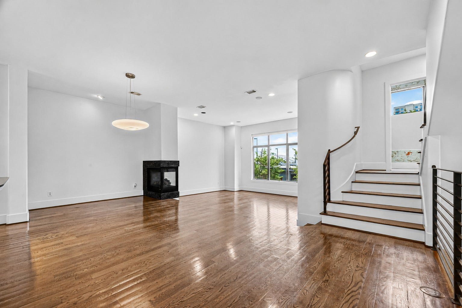 1110 Autrey Street, #C, Houston, TX 77006 Spacious living area with elegant hardwood floors, a modern fireplace, large windows for natural light, and a stylish curved staircase.