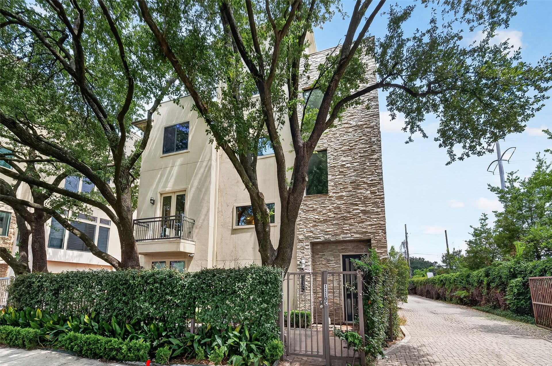 1110 Autrey Street, #C, Houston, TX 77006 Modern townhome featuring a striking stone facade and private balcony, set amidst lush greenery and mature trees.