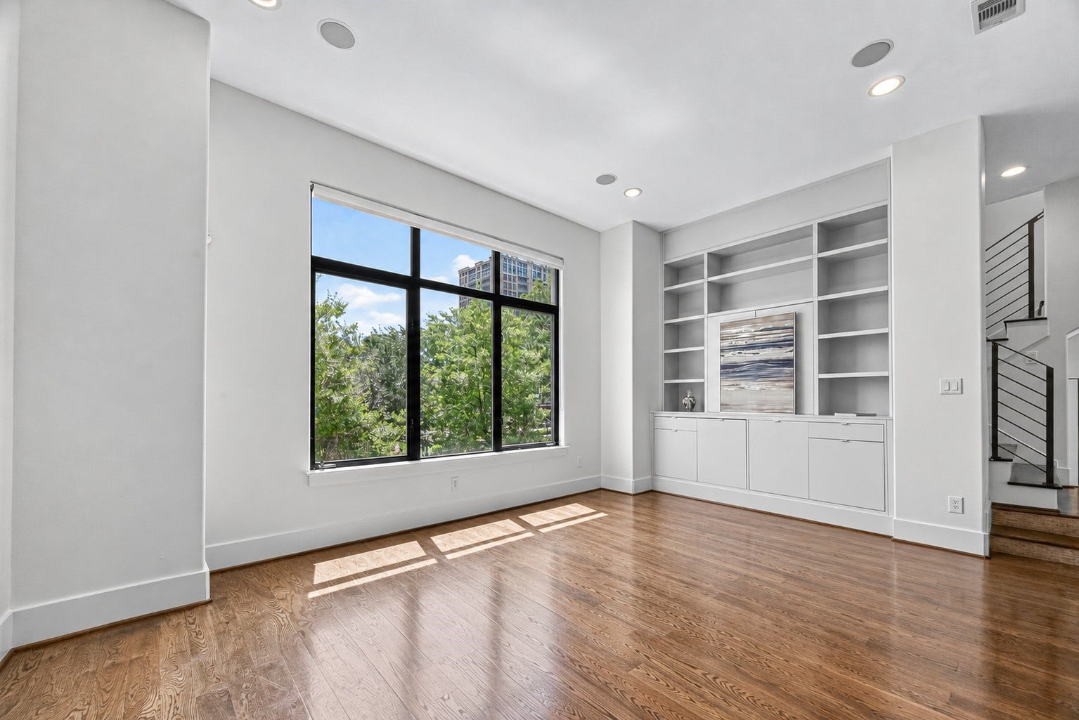 1110 Autrey Street, #C, Houston, TX 77006 Sunlit living room with large windows showcasing lush greenery, elegant built-in shelving, and rich hardwood floors.