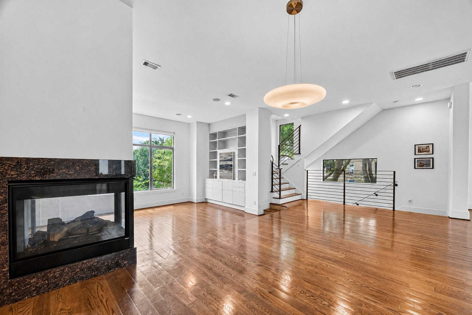 1110 Autrey Street, #C, Houston, TX 77006 Elegant open-concept living space featuring rich hardwood floors, a modern gas fireplace, large windows for natural light, built-in shelving, and a sleek staircase with contemporary railing.