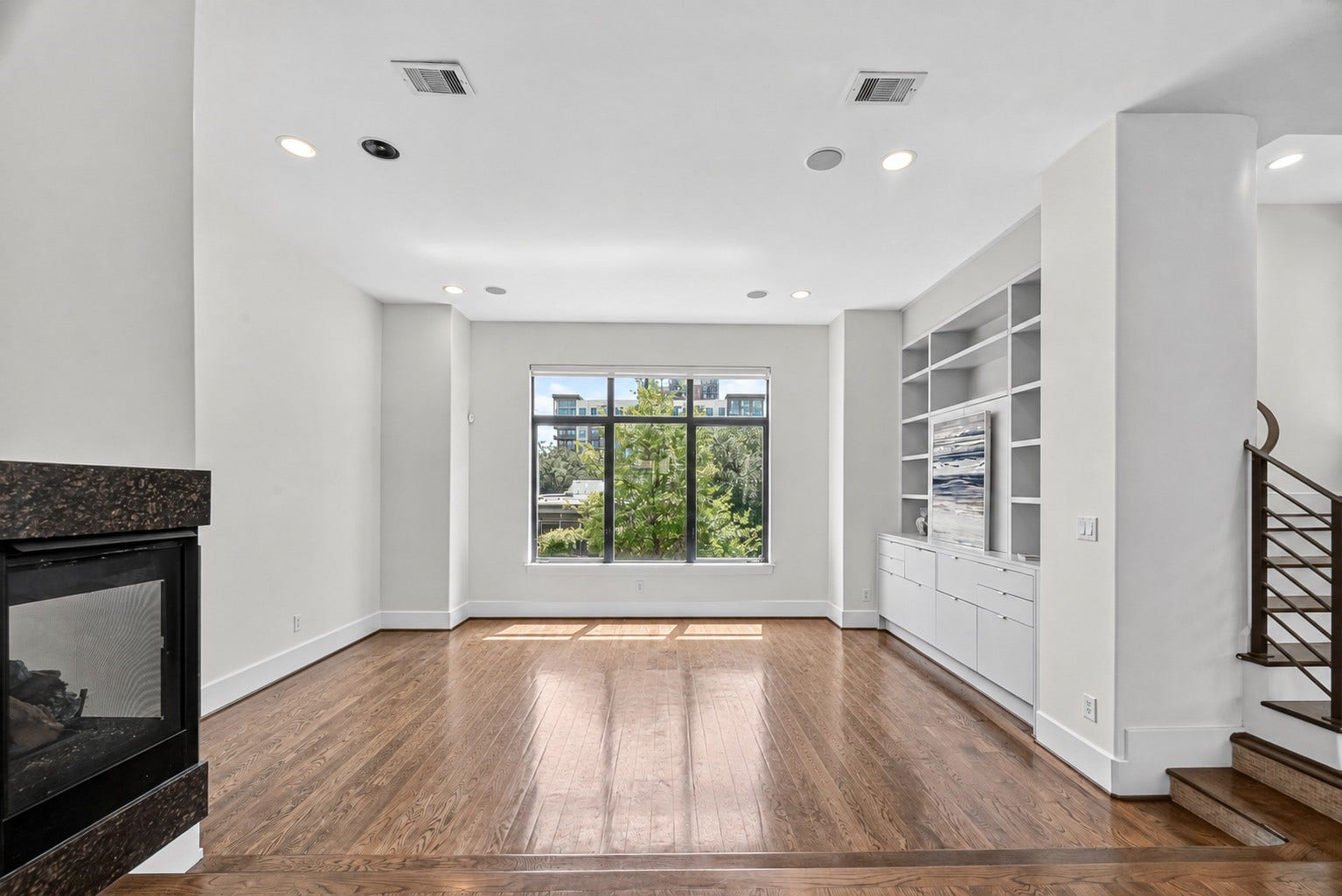 1110 Autrey Street, #C, Houston, TX 77006 Bright and spacious living area with hardwood floors, a cozy fireplace, and built-in shelving, complemented by a large window offering natural light and views of greenery.