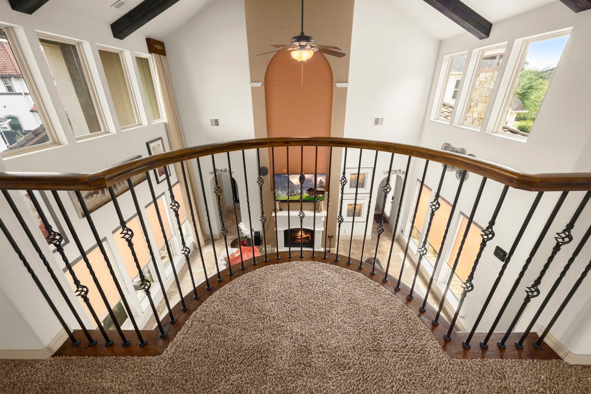 5103 Jackson Ponds Court, Sugar Land, TX 77479 This photo showcases an elegant, open-concept home with a view from the top of a staircase. It features a curved, wrought iron railing overlooking a spacious living area below. The area is well-lit with large windows and includes a cozy fireplace, creating a warm and inviting atmosphere.