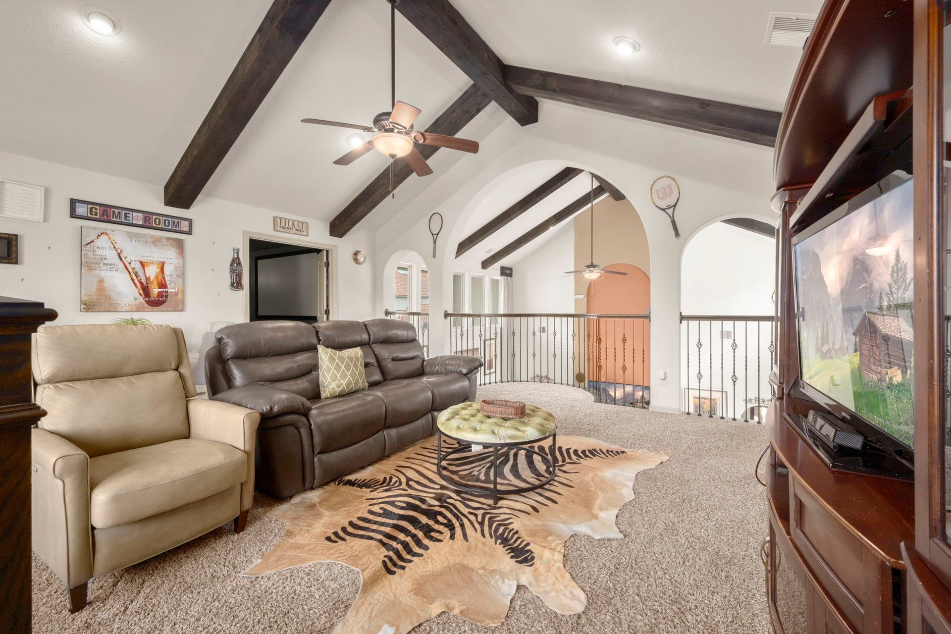 5103 Jackson Ponds Court, Sugar Land, TX 77479 This inviting game room features a vaulted ceiling with exposed beams, plush seating, and a cozy atmosphere. A large TV and stylish decor, including a zebra-patterned rug, enhance the space, making it perfect for relaxation and entertainment.