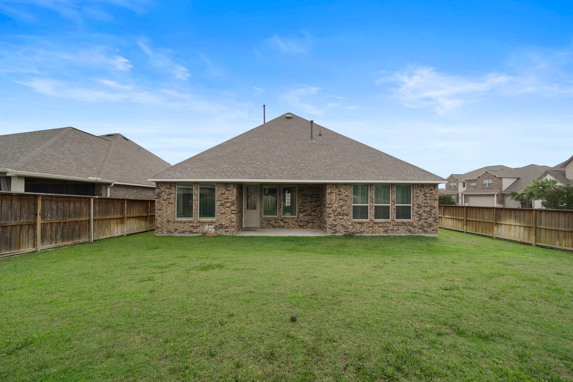The rear elevation showcases the homes attractive brick exterior, multiple windows, and covered patio overlooking a large fenced lawn. With plenty of room for outdoor furniture, games, gardening, or entertaining, the backyard provides a versatile setting ready to accommodate a wide variety of outdoor living ideas.