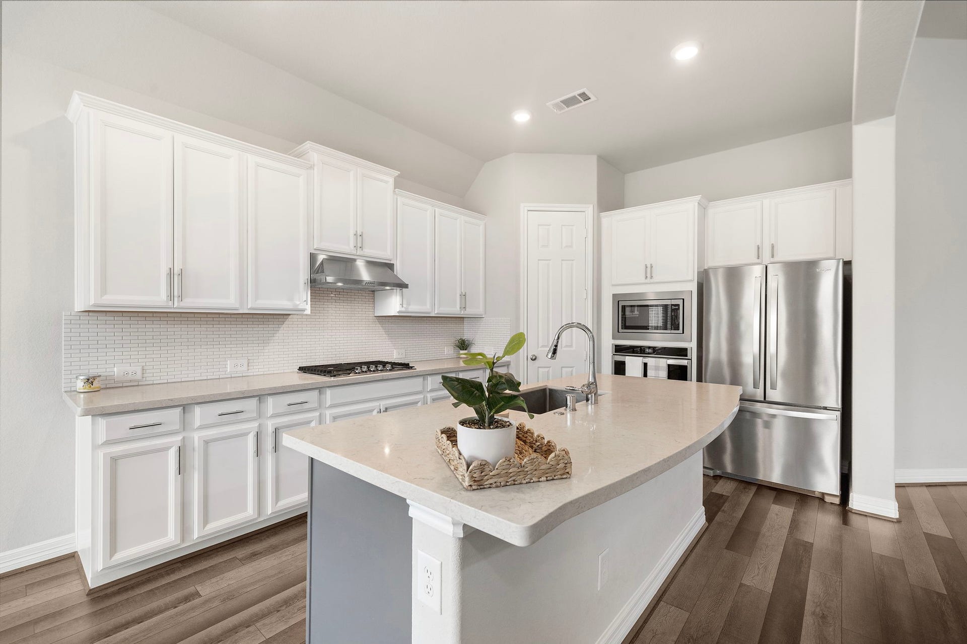 The spacious kitchen pairs timeless white cabinetry with stainless steel appliances, sleek counters, and a substantial center island ideal for meal preparation and casual gathering. A built-in oven and microwave, gas cooktop, modern vent hood, and abundant cabinetry provide the functionality buyers appreciate in a beautifully finished space.