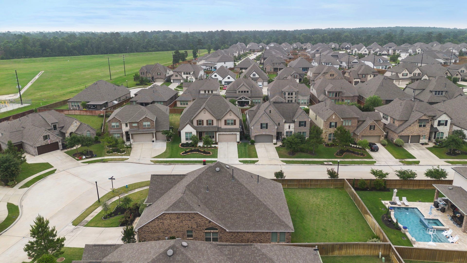 A sweeping aerial view showcases the larger neighborhood, with rows of attractive homes, landscaped yards, sidewalks, and established streets extending toward nearby green space. The image highlights the communitys cohesive residential character and provides helpful perspective on the homes setting within the surrounding area.