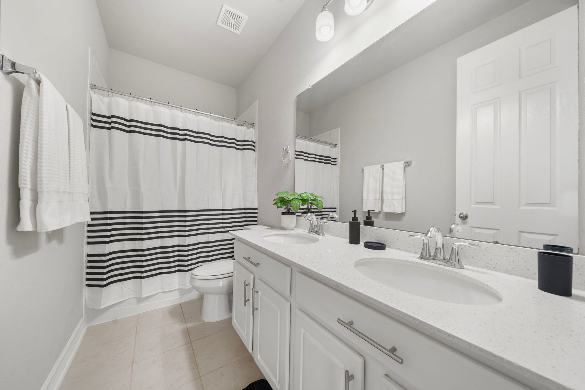 The full bathroom features a spacious double-sink vanity with abundant cabinetry, bright countertops, a large wall mirror, and modern fixtures. A tub and shower combination provides everyday convenience, while neutral tile flooring and crisp finishes give the space a clean, timeless appearance that is easy to personalize.