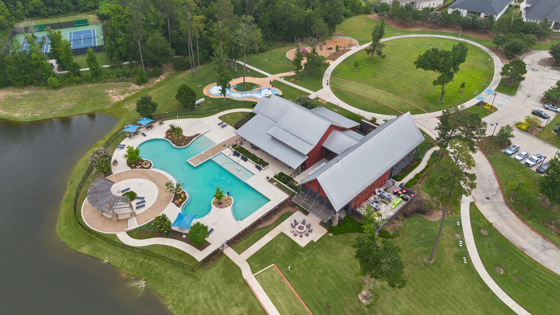An impressive aerial view showcases the community amenity center surrounded by lush green space. Residents can enjoy a resort-style swimming pool, splash area, playground, tennis courts, walking paths, gathering spaces, and a scenic pond, creating an exceptional environment for recreation, relaxation, and an active outdoor lifestyle.