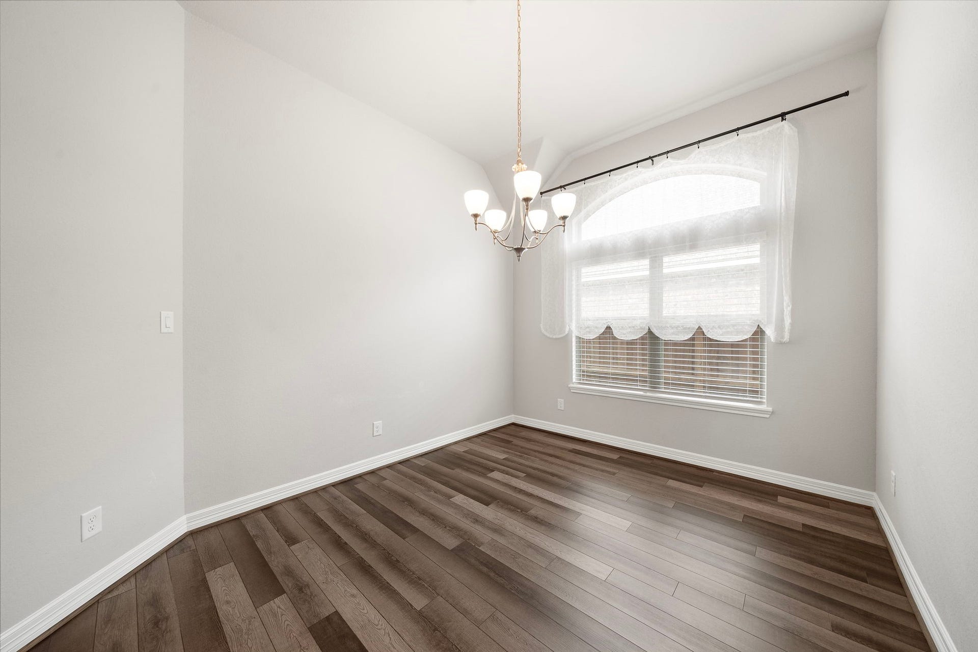 This inviting dining space features warm wood-look flooring, a graceful chandelier, and a large arched window that brings in abundant natural light. Neutral finishes create a clean backdrop for a variety of decorating styles, while the rooms proportions provide ample space for a full dining table and additional furnishings.