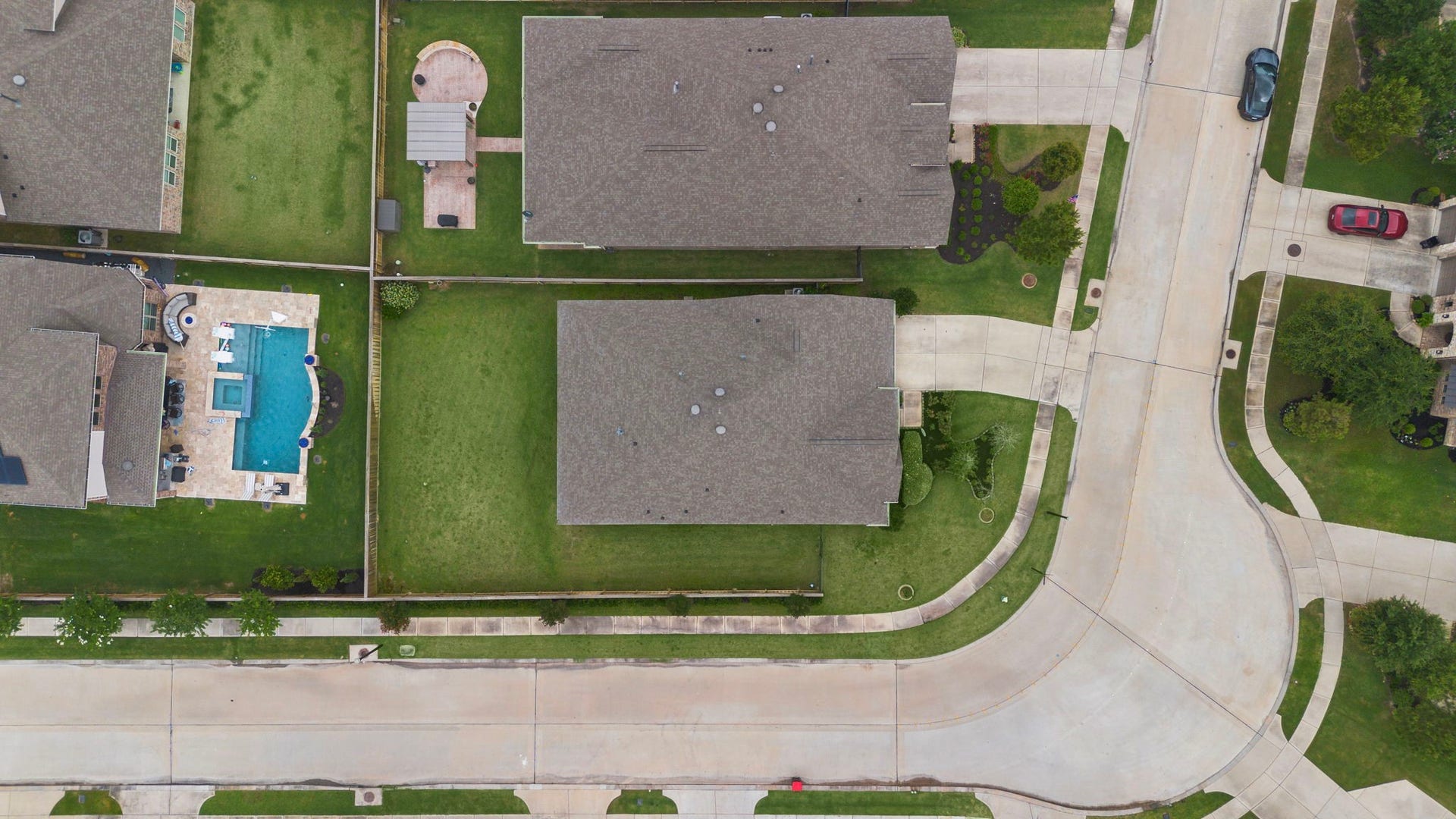 This overhead aerial view highlights the propertys generous lot, expansive fenced backyard, driveway, landscaped front yard, and prominent position along the curved residential street. The birds-eye perspective clearly shows the homes footprint and substantial outdoor space, offering a helpful look at the propertys layout and relationship to neighboring homes.