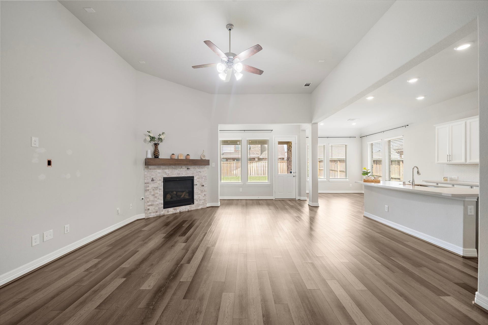 The open-concept living area offers an impressive combination of space, natural light, and effortless flow. A stone-accented fireplace creates a warm focal point, while expansive windows and high ceilings enhance the bright atmosphere. The adjoining kitchen and dining spaces make everyday living and entertaining feel seamless.
