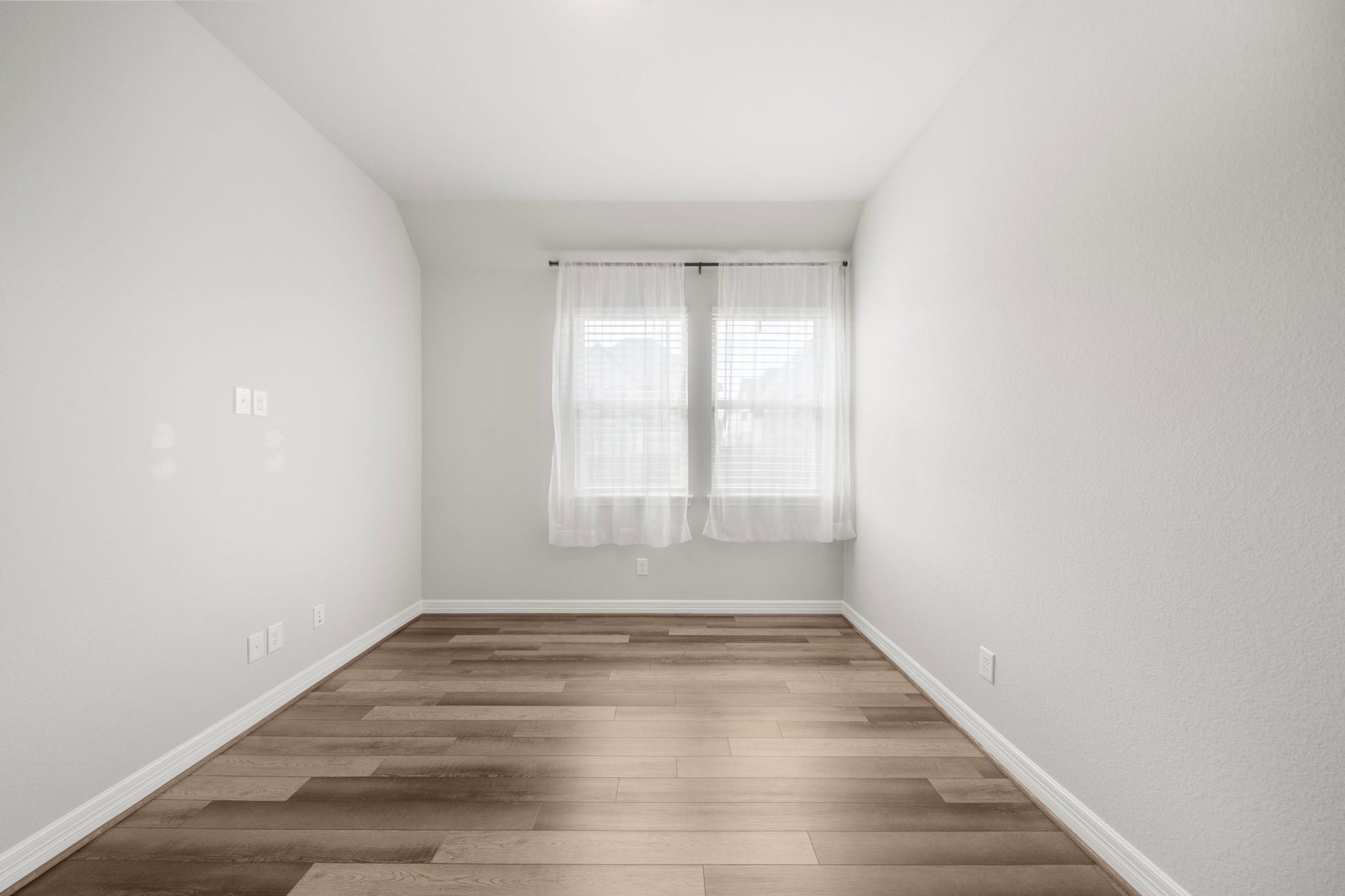 A bright, flexible room offers warm wood-look flooring, neutral walls, and twin windows that fill the space with natural light. The long, open layout provides excellent versatility for a home office, study, sitting room, hobby space, or additional dining area, allowing the next owner to tailor it to their lifestyle.