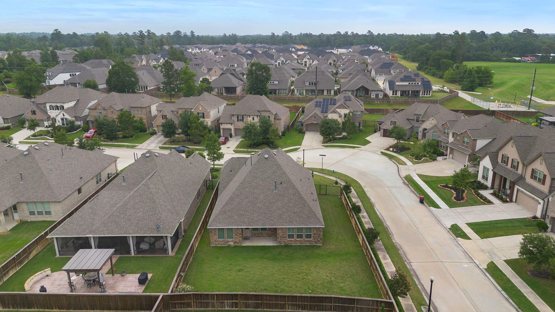 From above, the propertys generous backyard and residential setting come into clear view. The fenced lawn provides substantial private outdoor space, while the surrounding neighborhood features attractive homes, sidewalks, established landscaping, and tree-lined areas that enhance the overall sense of community.
