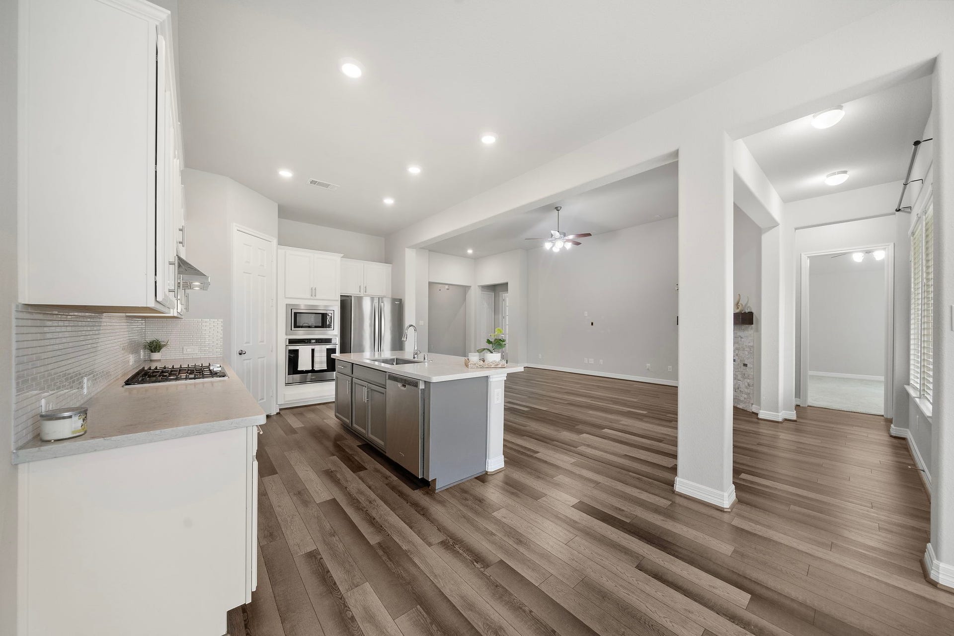This wide-angle view captures the seamless flow between the kitchen and adjoining living areas. Rich wood-look flooring extends throughout the open floor plan, while recessed lighting, a generous island, stainless steel appliances, and abundant cabinetry create a bright, connected space perfectly suited for daily living and entertaining.