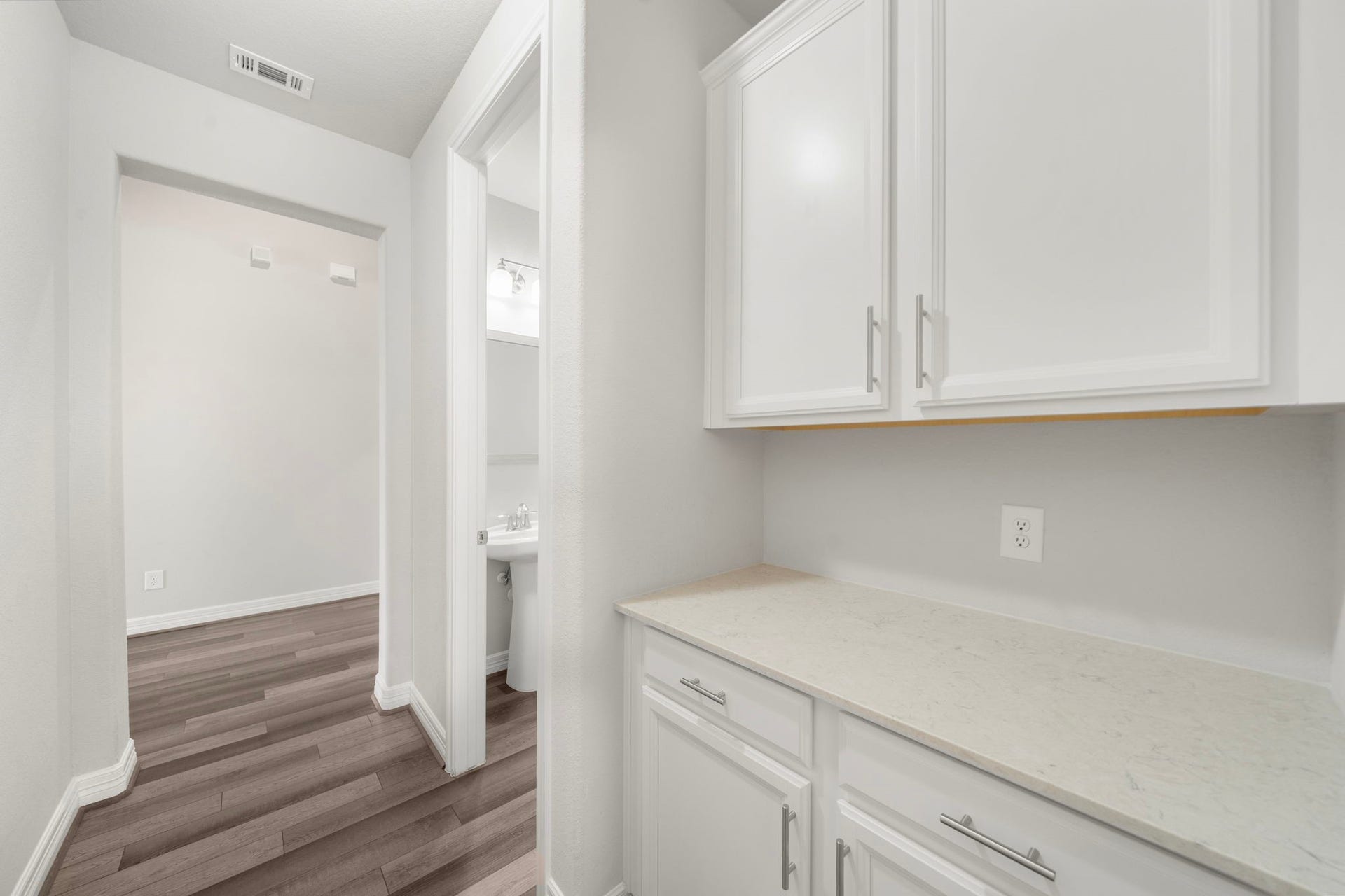 A practical built-in storage area adds valuable function with upper and lower cabinetry, countertop workspace, and an electrical outlet for small appliances or charging needs. Positioned near an additional bath and hallway, this flexible space can serve as a beverage station, household organization area, linen storage, or everyday drop zone.