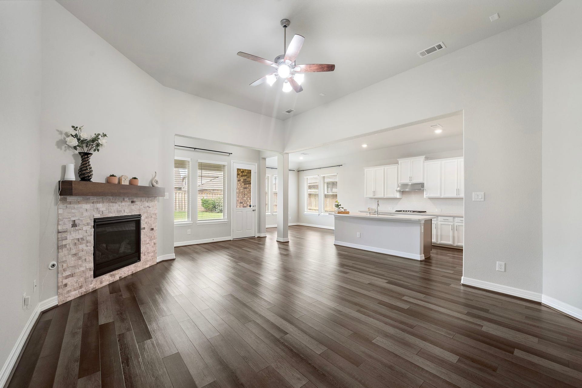 Spacious and inviting, the main living area features high ceilings, abundant natural light, and wide-plank wood-look flooring. A beautiful stone fireplace with a rich wood mantel anchors the room, while the open connection to the kitchen creates a comfortable gathering space perfect for relaxing, entertaining, or everyday living.