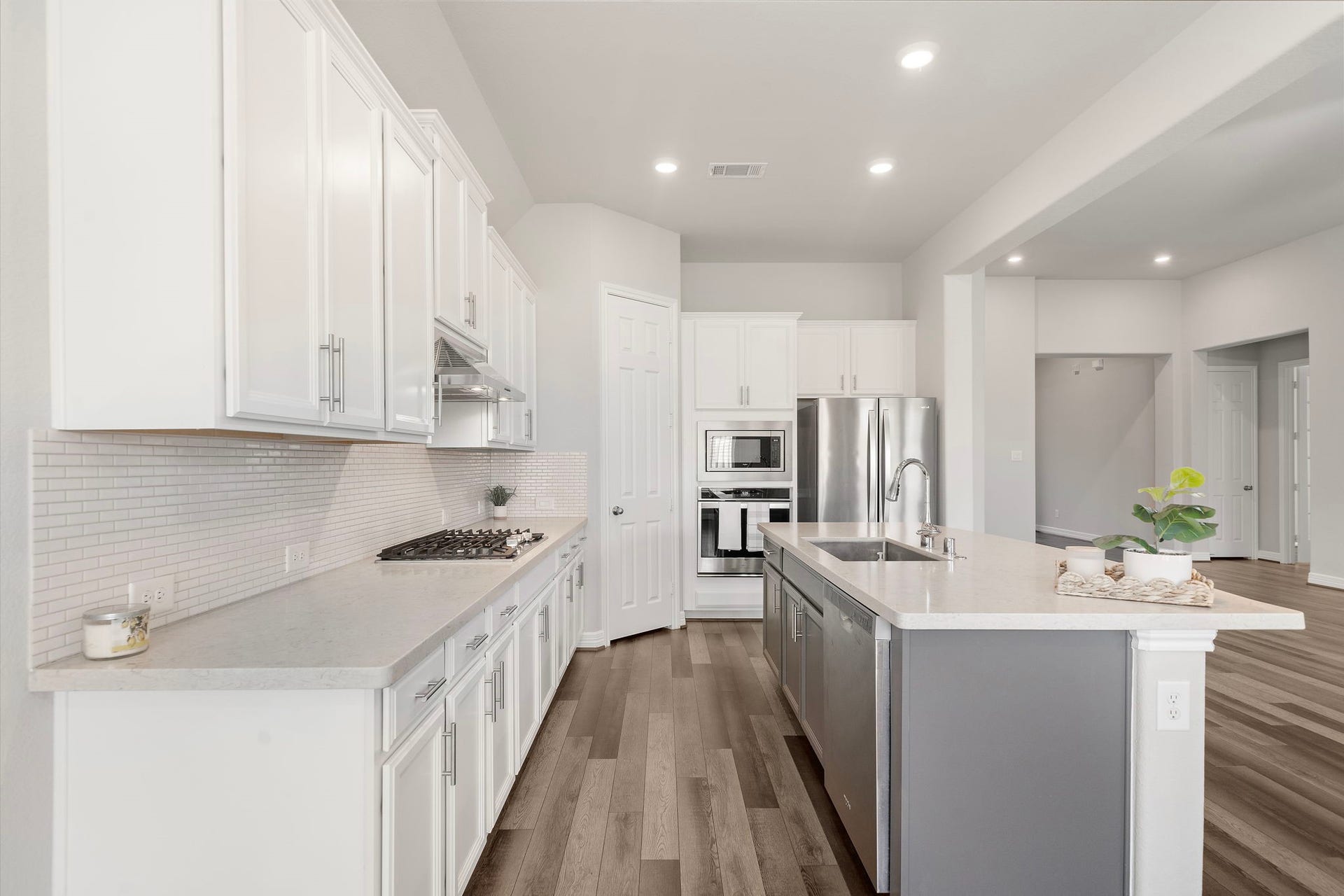 From this angle, the kitchens thoughtful layout is on full display with extensive counter space, white cabinetry, stainless steel appliances, and a large contrasting island. The built-in microwave and oven, gas cooktop, undermount sink, and recessed lighting combine convenience with a clean, contemporary aesthetic.