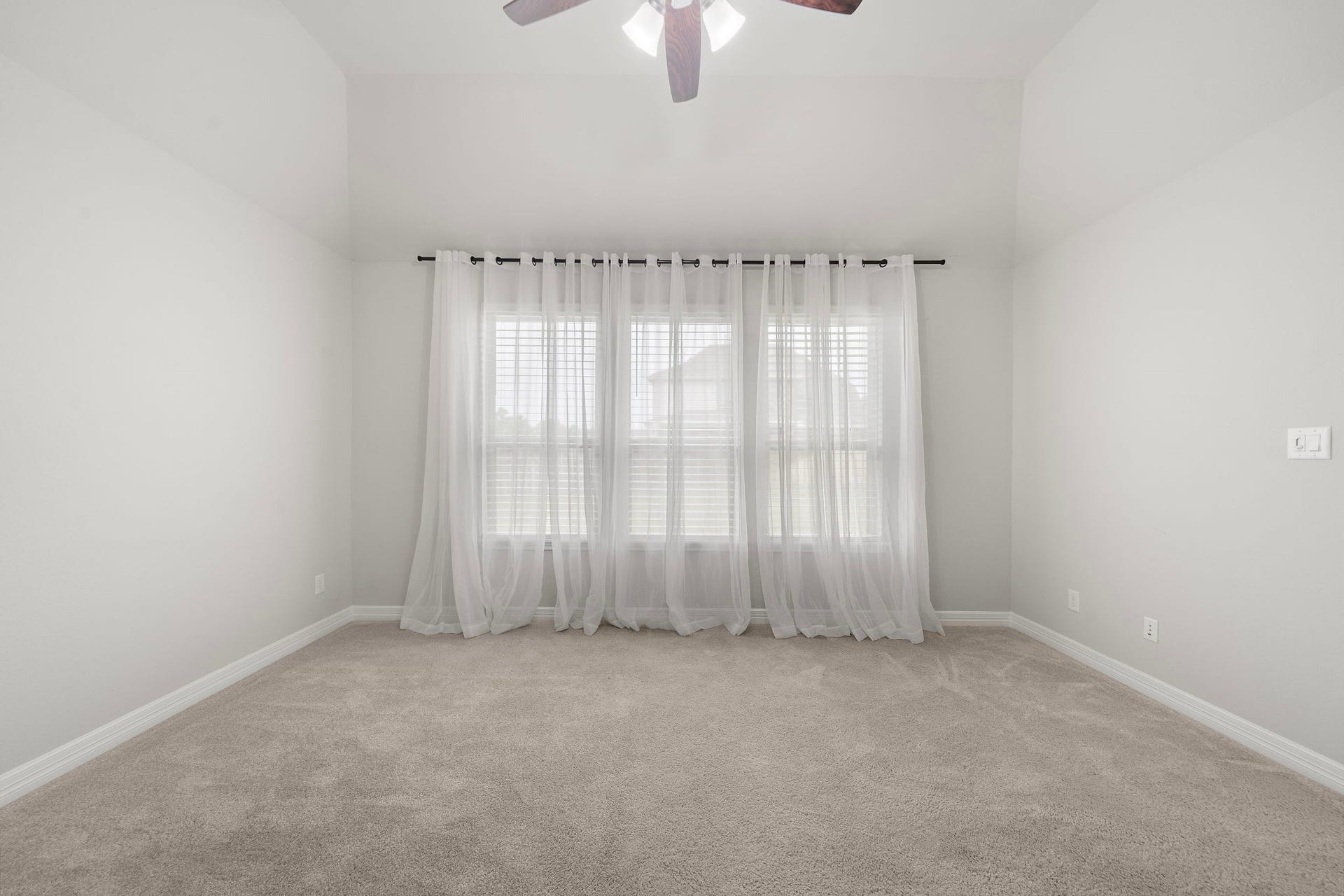 Another view of the primary bedroom highlights its impressive size, high ceiling, soft carpeting, and abundant natural light. A ceiling fan enhances comfort, while the room provides excellent flexibility for a king-size bed, sitting area, dressers, and additional furnishings without sacrificing an open, relaxing atmosphere.