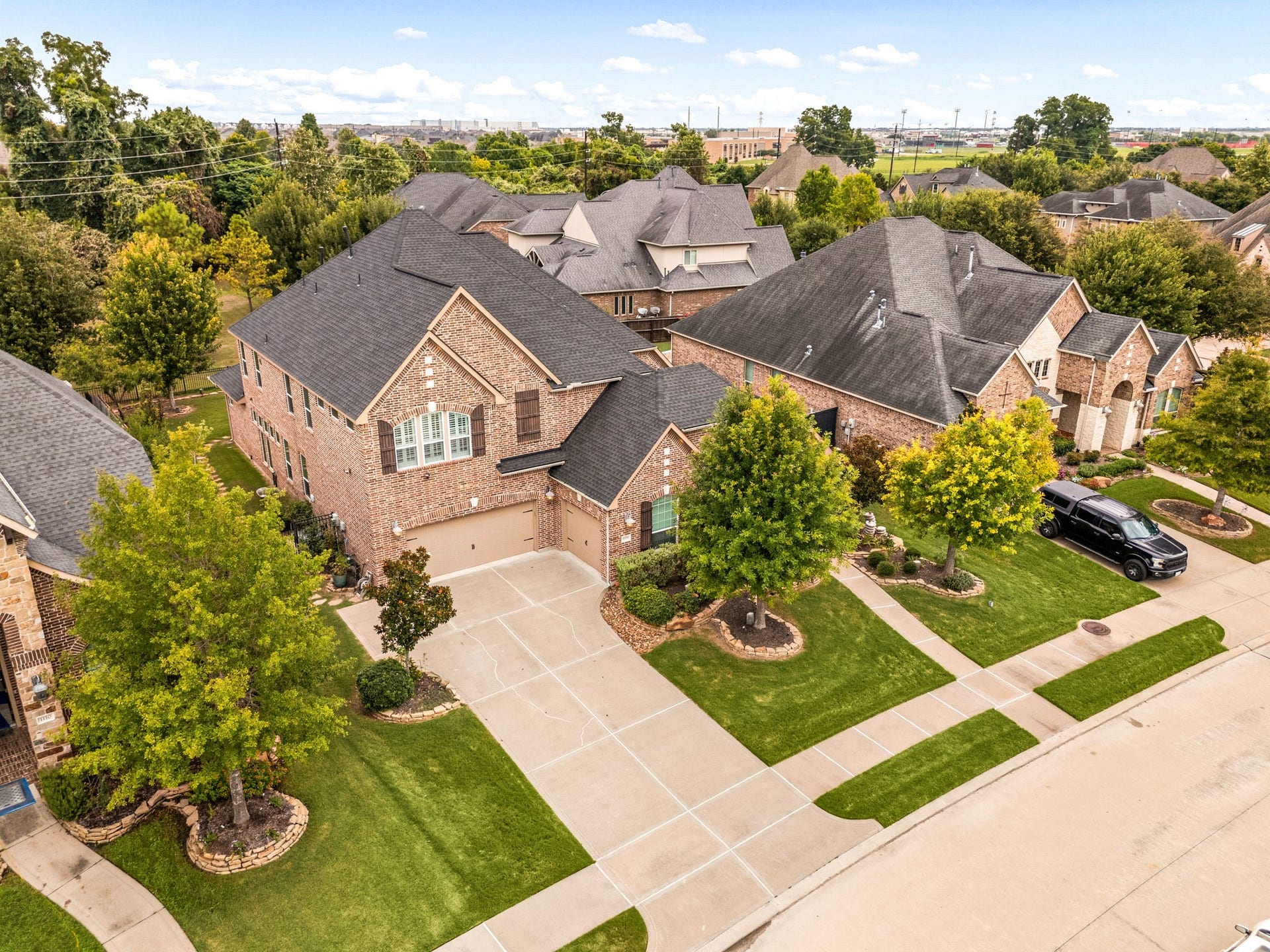 An aerial view of 1106 River Bow Drive showcases the homes three-car garage and established setting in Richmonds Harvest Green community, with nearby Travis High School visible in the surrounding area.