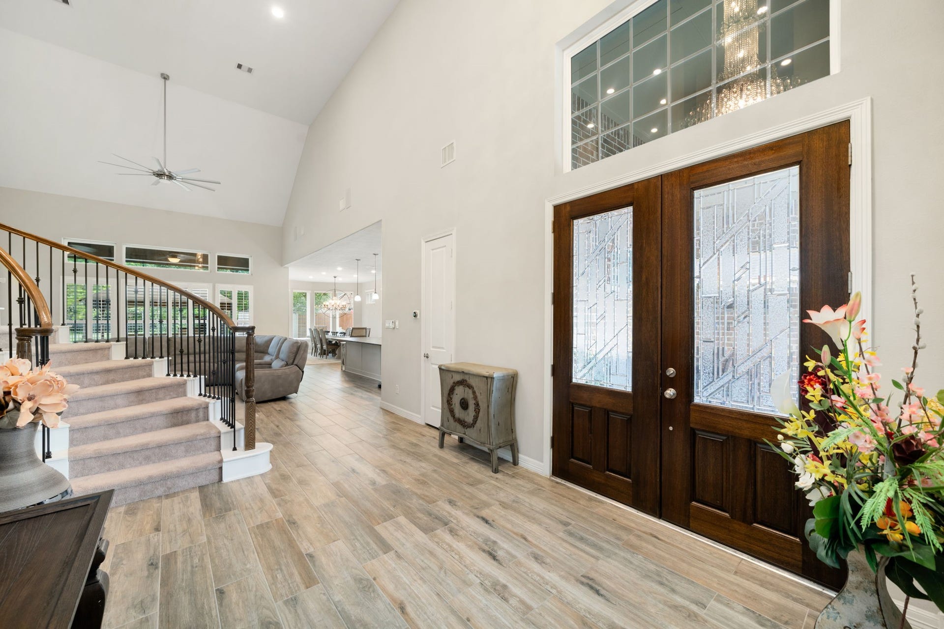 Step inside to a dramatic two-story foyer with soaring ceilings, wood-look tile flooring, and a curved staircase with wrought-iron balusters  setting an open, airy tone for the home.