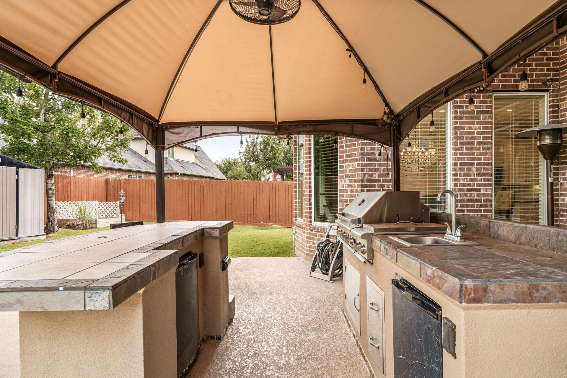 A closer look at the outdoor kitchen's stainless grill, sink, and generous counter space, set beneath a covered patio structure.