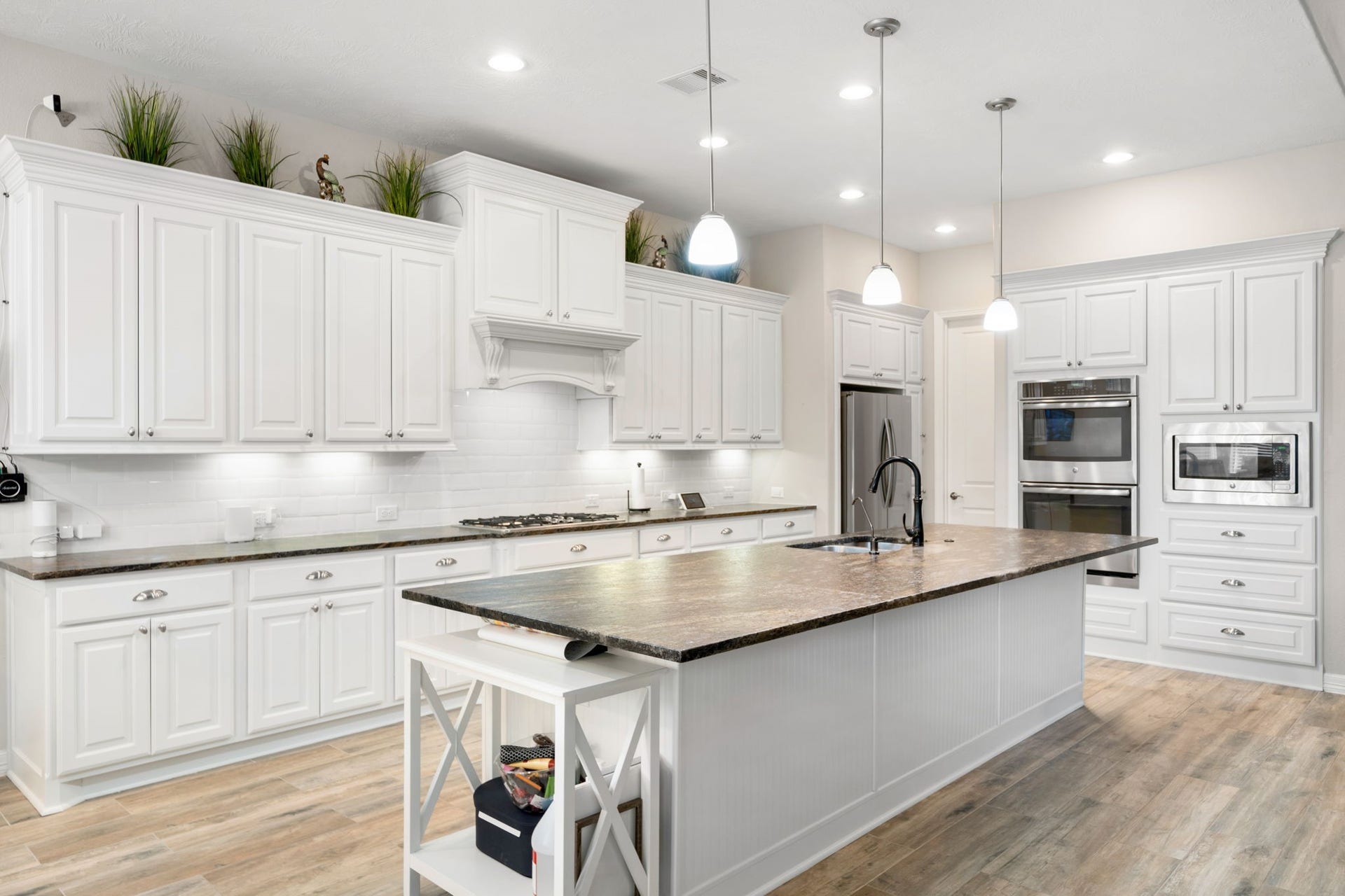 The kitchen features abundant white cabinetry, granite countertops, and stainless steel appliances including a built-in double oven and microwave, all centered around a spacious island with sink.