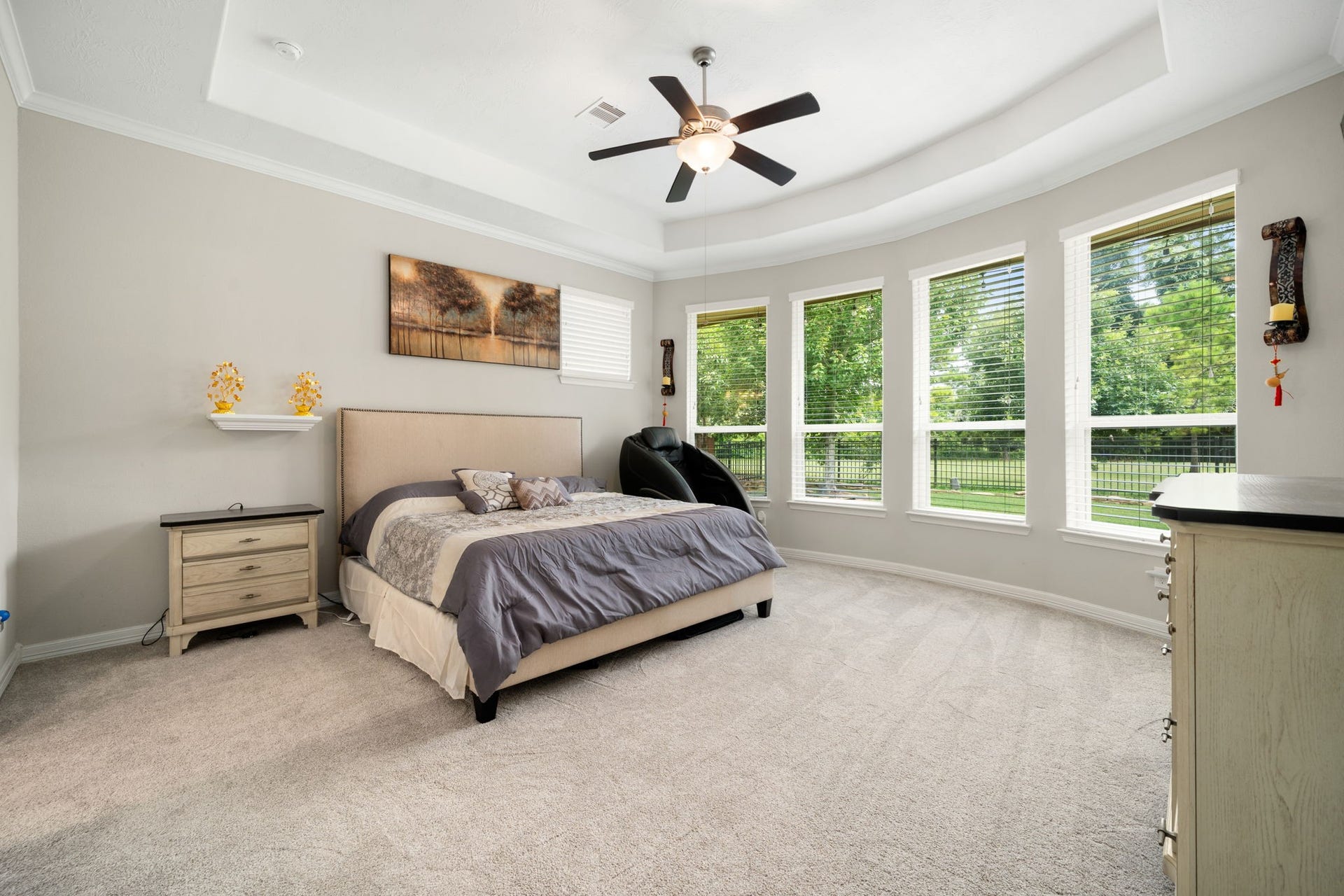 The primary bedroom offers a generously sized layout with a tray ceiling, plush carpet, and a wall of windows overlooking the backyard.