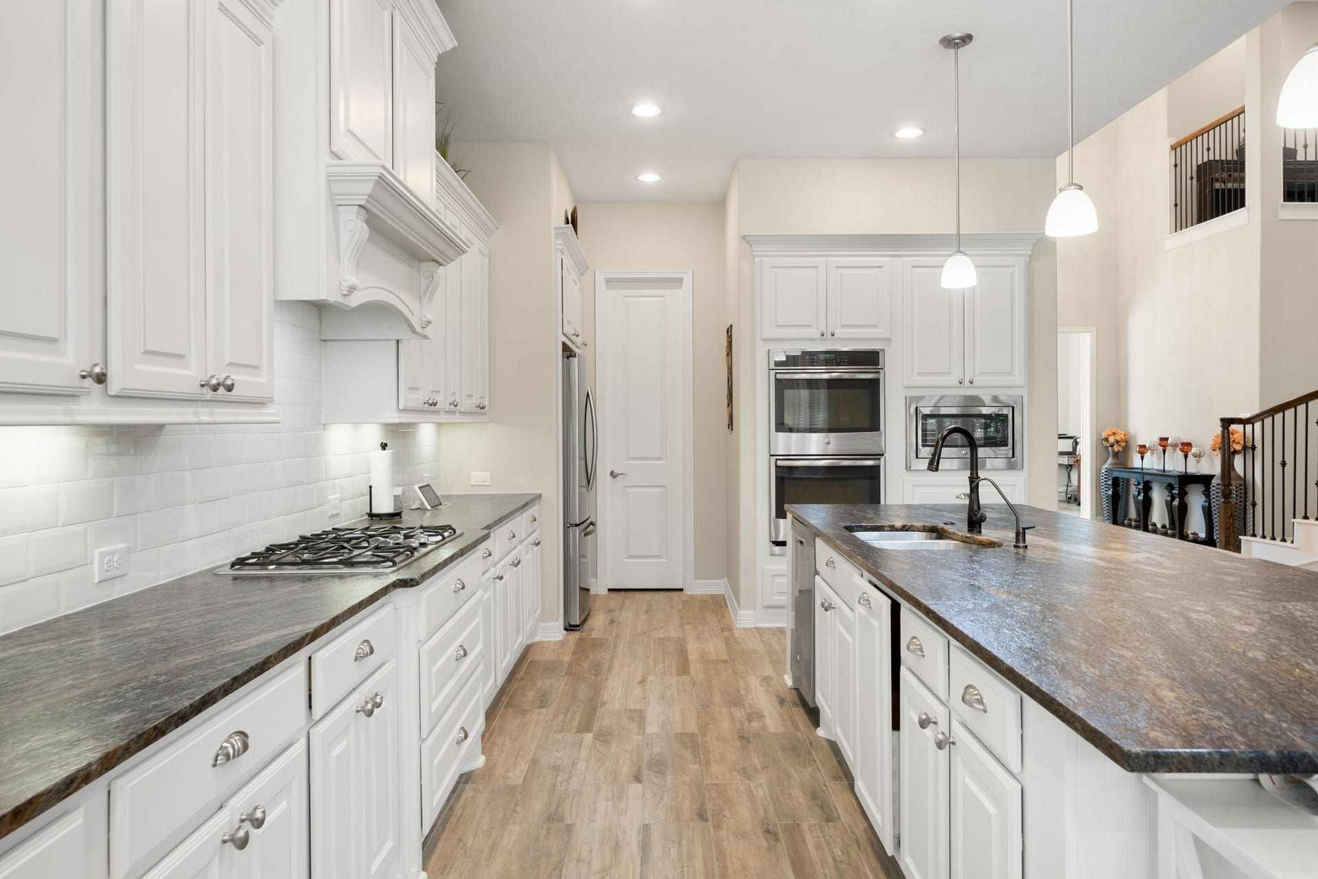 A gas cooktop and additional prep space line the perimeter counter, with a walk-in pantry and stainless refrigerator completing this well-appointed kitchen.